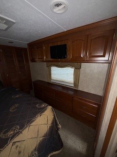 Spacious RV rental bedroom features a bed on the left, with ample wood storage, TV, and window on the right.. Keystone RV Alpine 2011