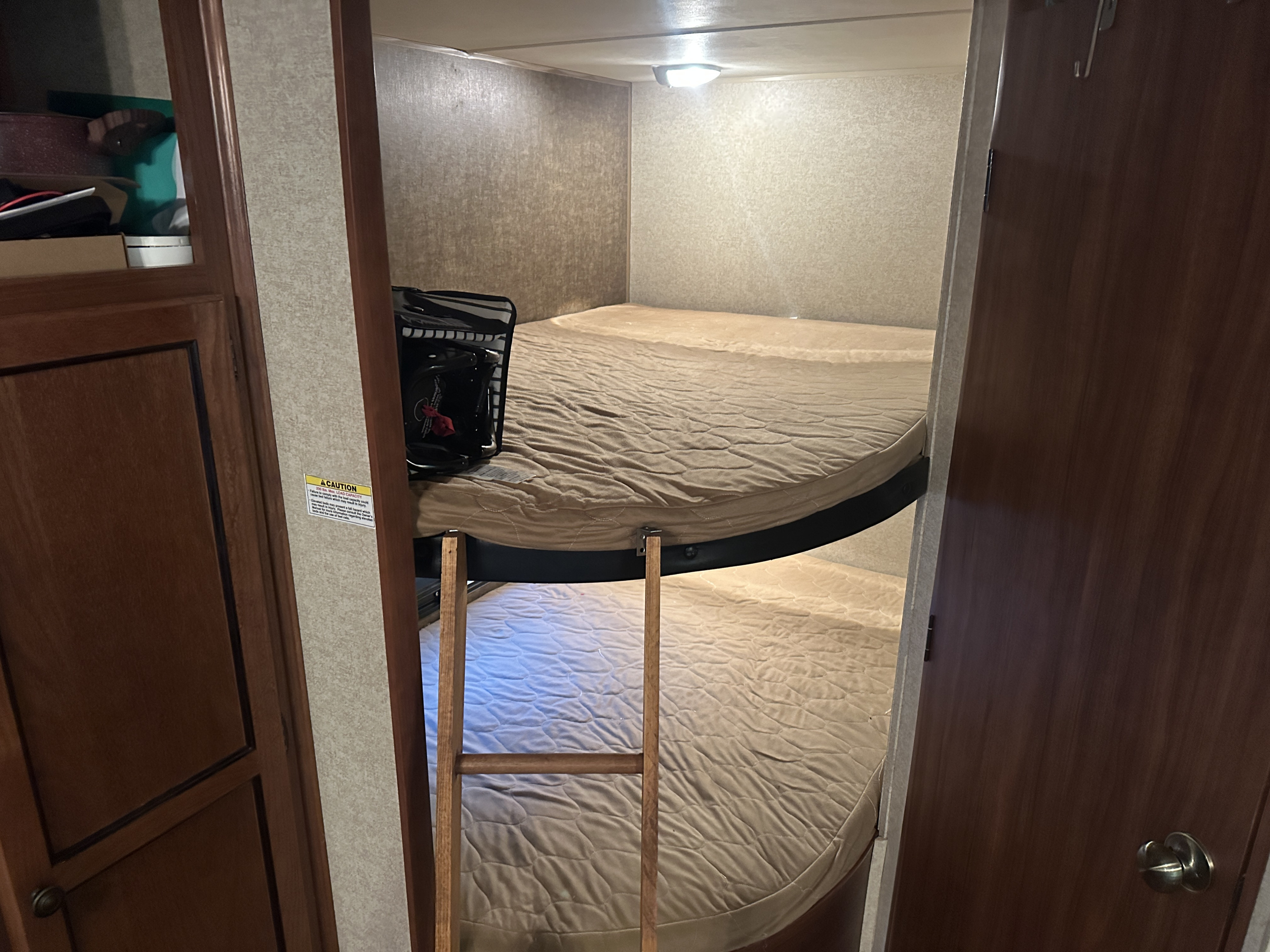Cozy RV rental bunk beds, featuring two stacked beds with textured mattresses and a wooden ladder for access.. Heartland RVs Trail Runner 2014