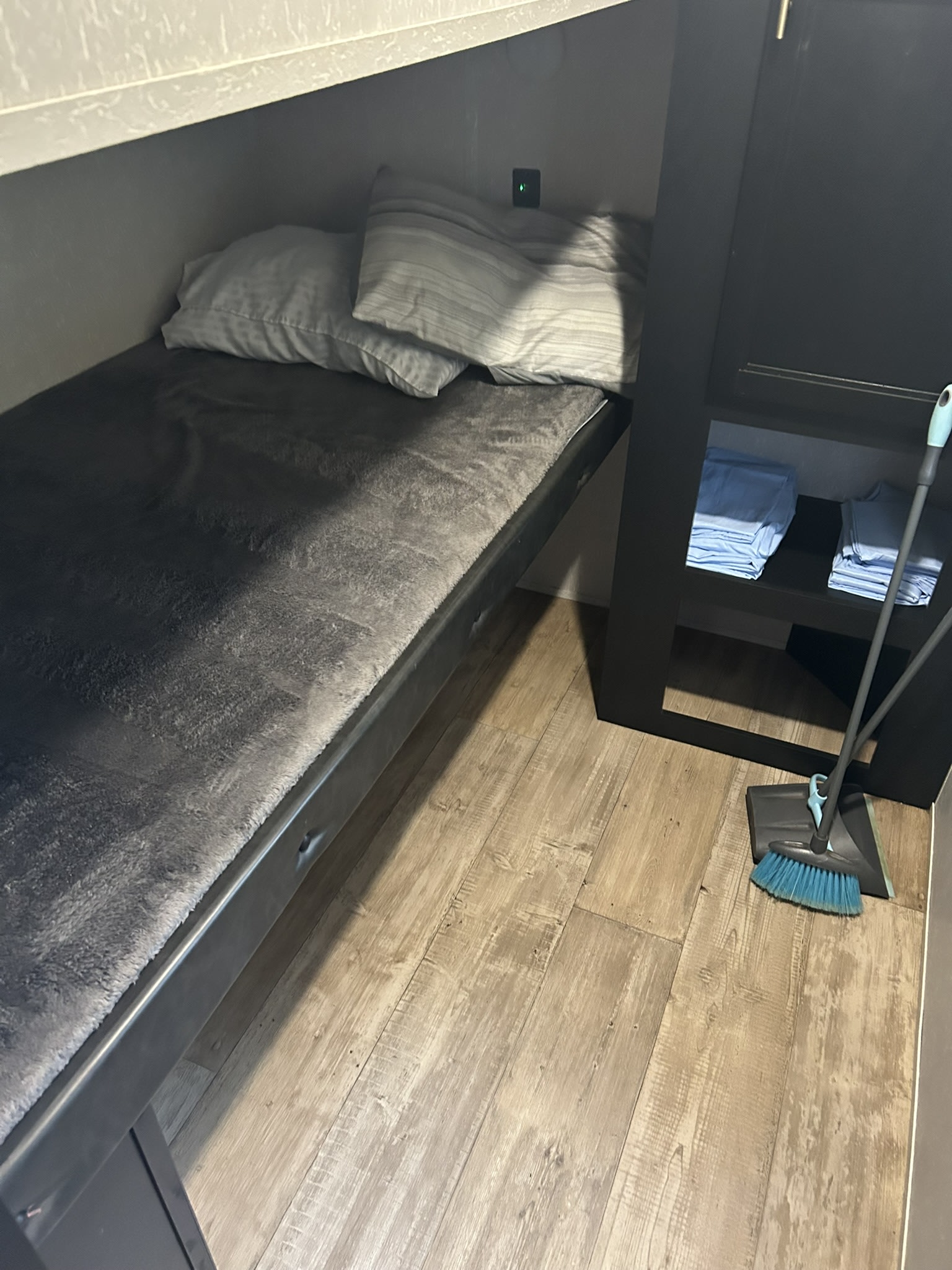 This RV rental features a compact bunk bed with a grey blanket, storage cubbies with blue linens, and a broom nearby.. Forest River Cherokee 2021