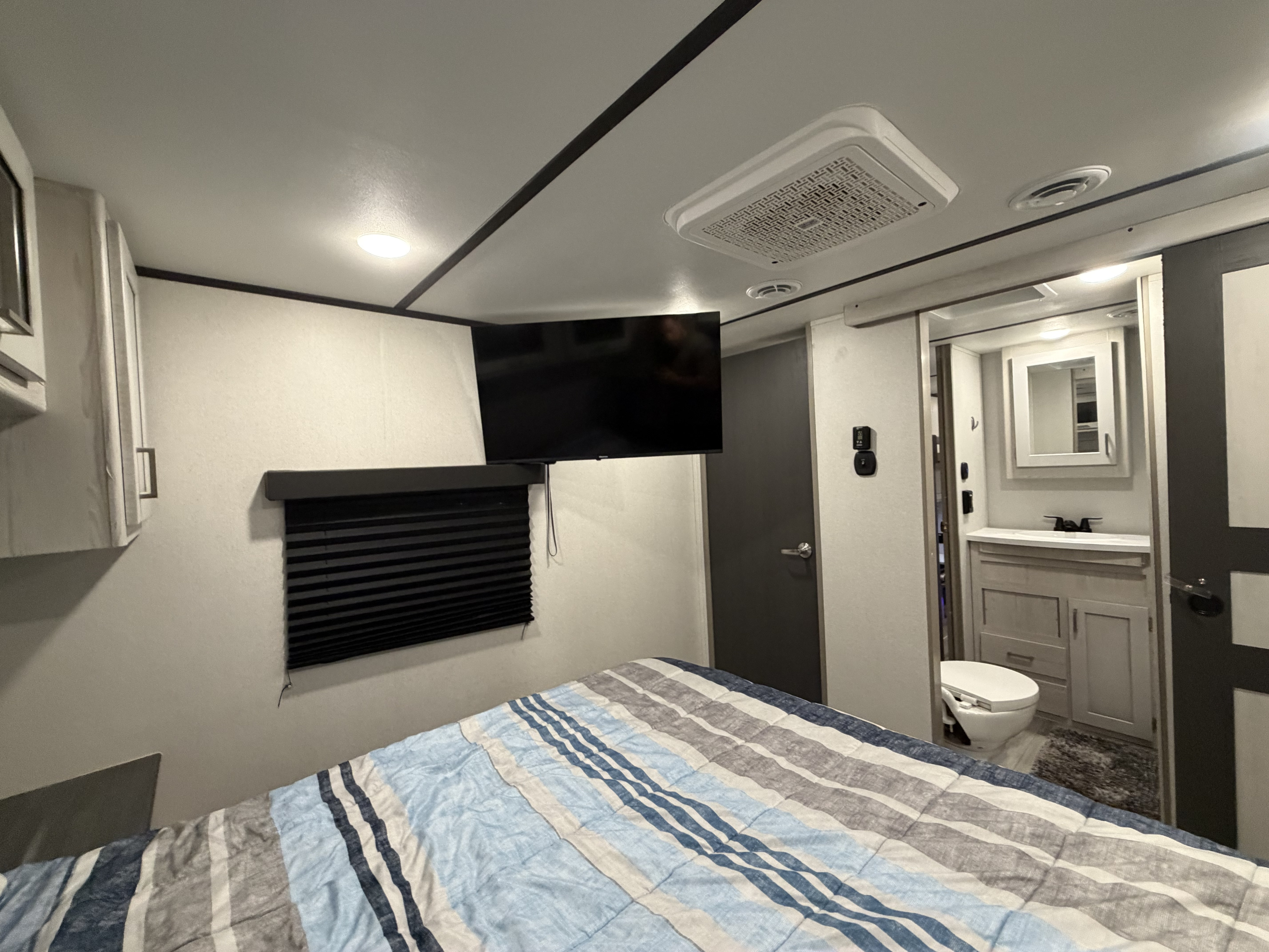 Inside an RV rental: cozy bedroom with striped bedding, TV, AC, and a convenient en-suite bathroom.. Keystone RV Sprinter 2022