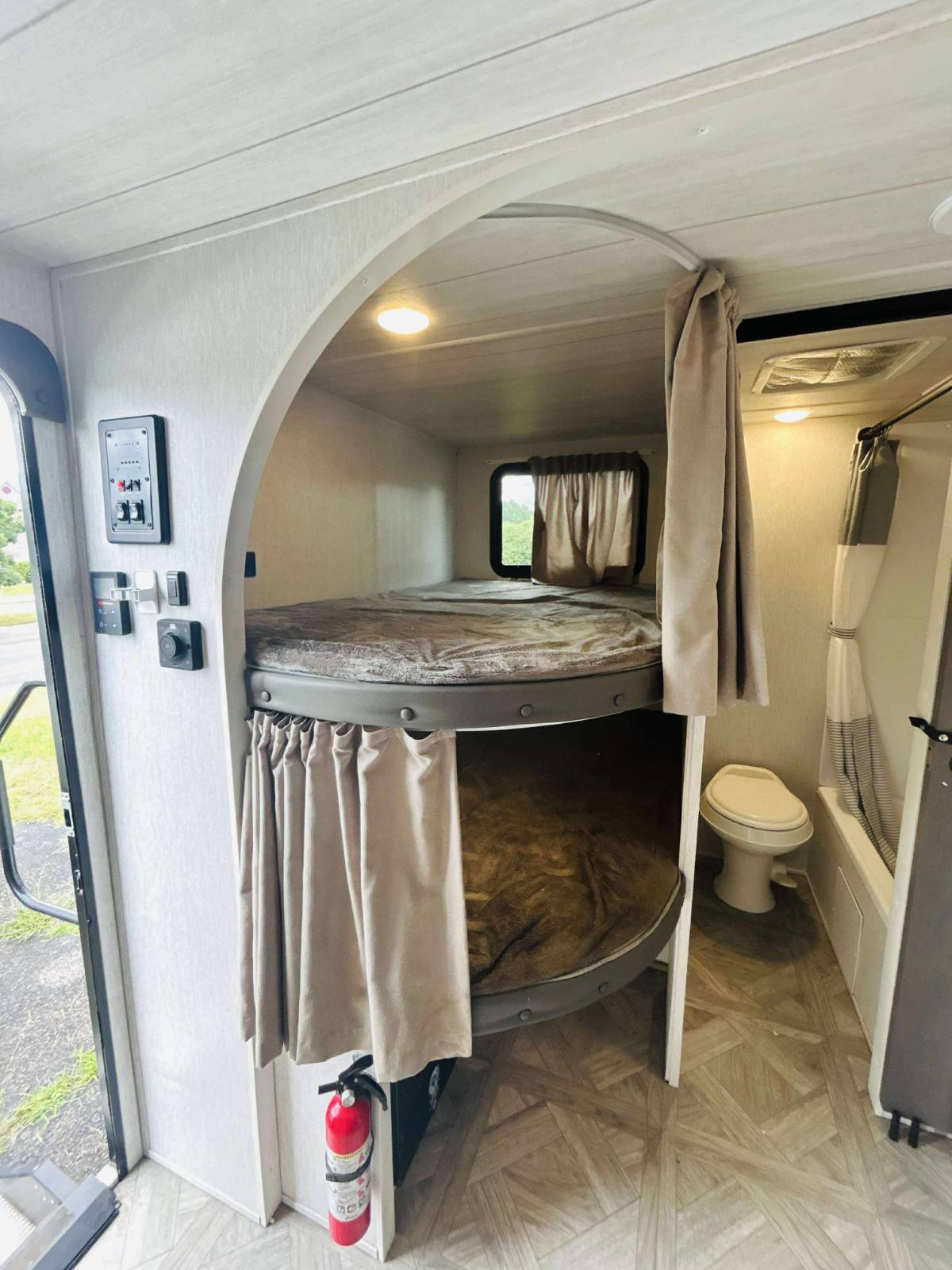 Inside an rv rental: space-saving bunk beds with privacy curtains, a compact toilet/shower, and a fire extinguisher for safety.. Forest River Wildwood X-Lite 2024