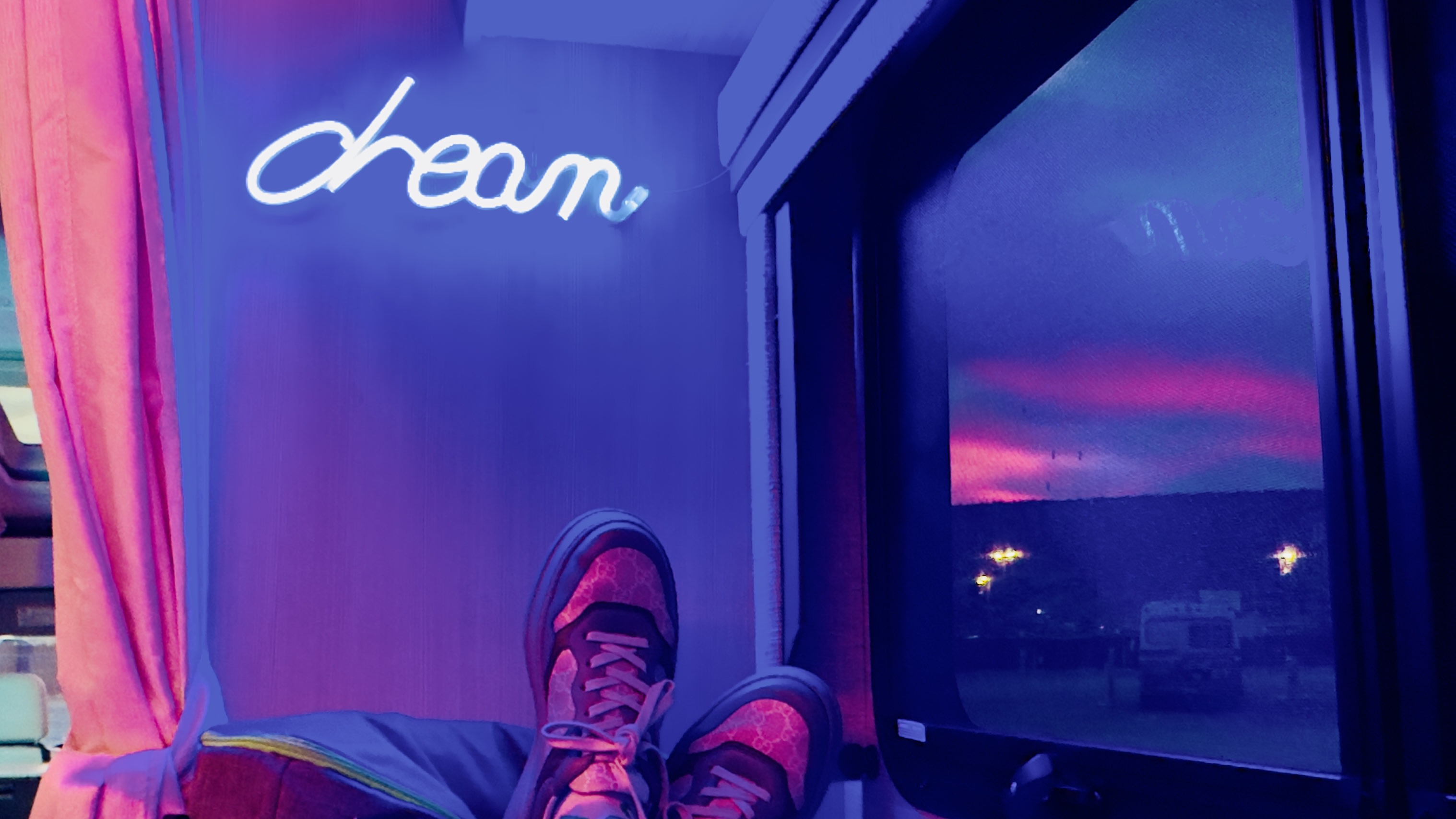 Feet up in an RV rental, admiring a "dream" neon sign and the stunning purple sunset from the window.. Thor Compass 2024