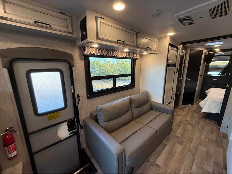 Explore this RV rental's inviting interior, featuring a comfortable sofa, kitchen storage, and a glimpse of the bedroom. Entry door on left.. Entegra Coach Odyssey 2022