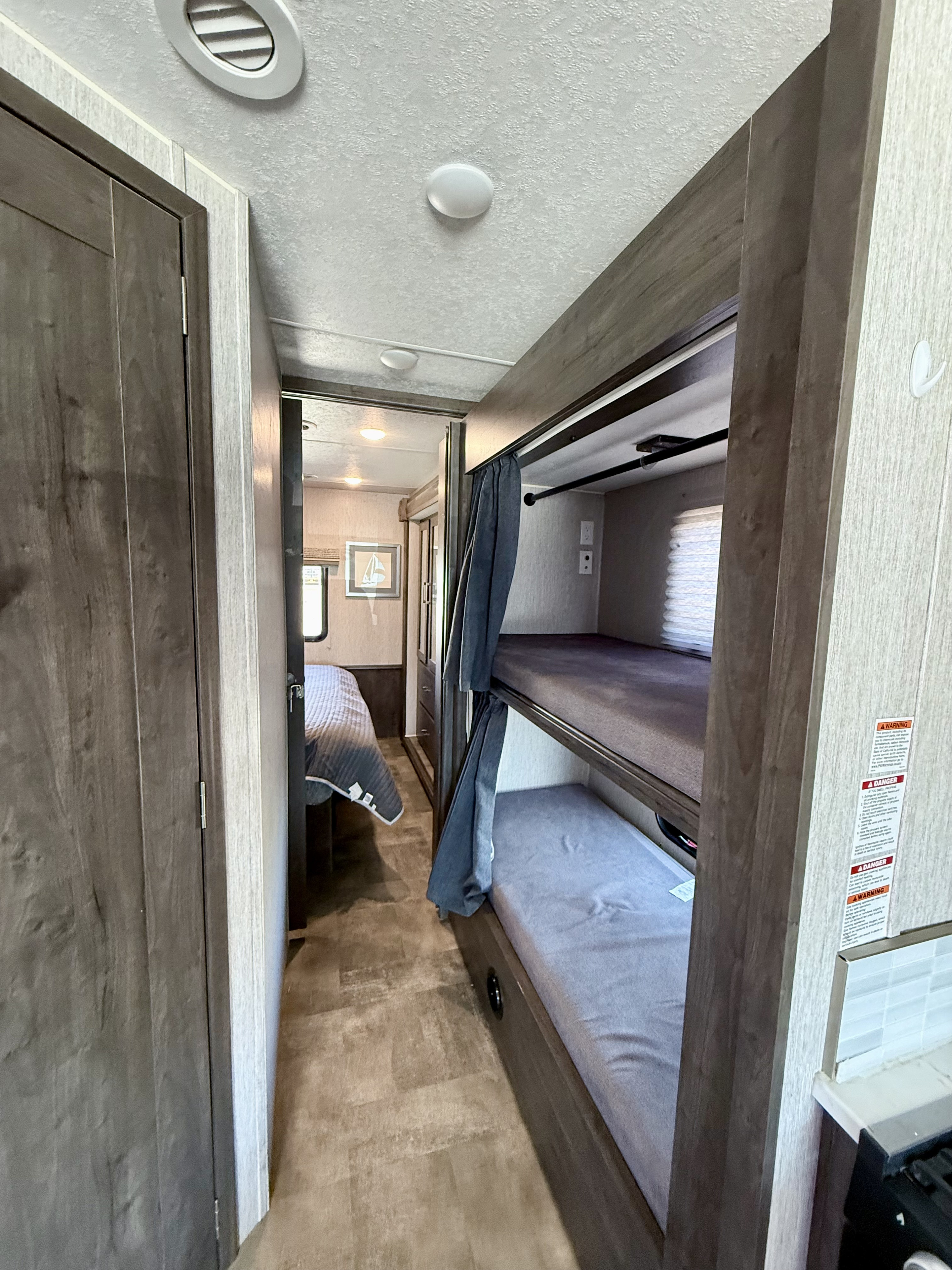 This RV rental interior features a hallway with bunk beds on the right and a private bedroom ahead, offering versatile sleeping arrangements.. Coachmen Pursuit 2022