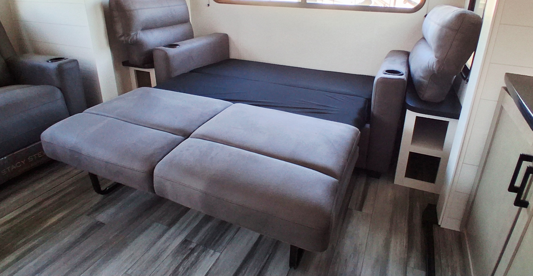 Gray convertible sofa bed in an RV rental, set up for sleeping. Features built-in cup holders in a modern interior.. Jayco Jay Flight SLX 2025