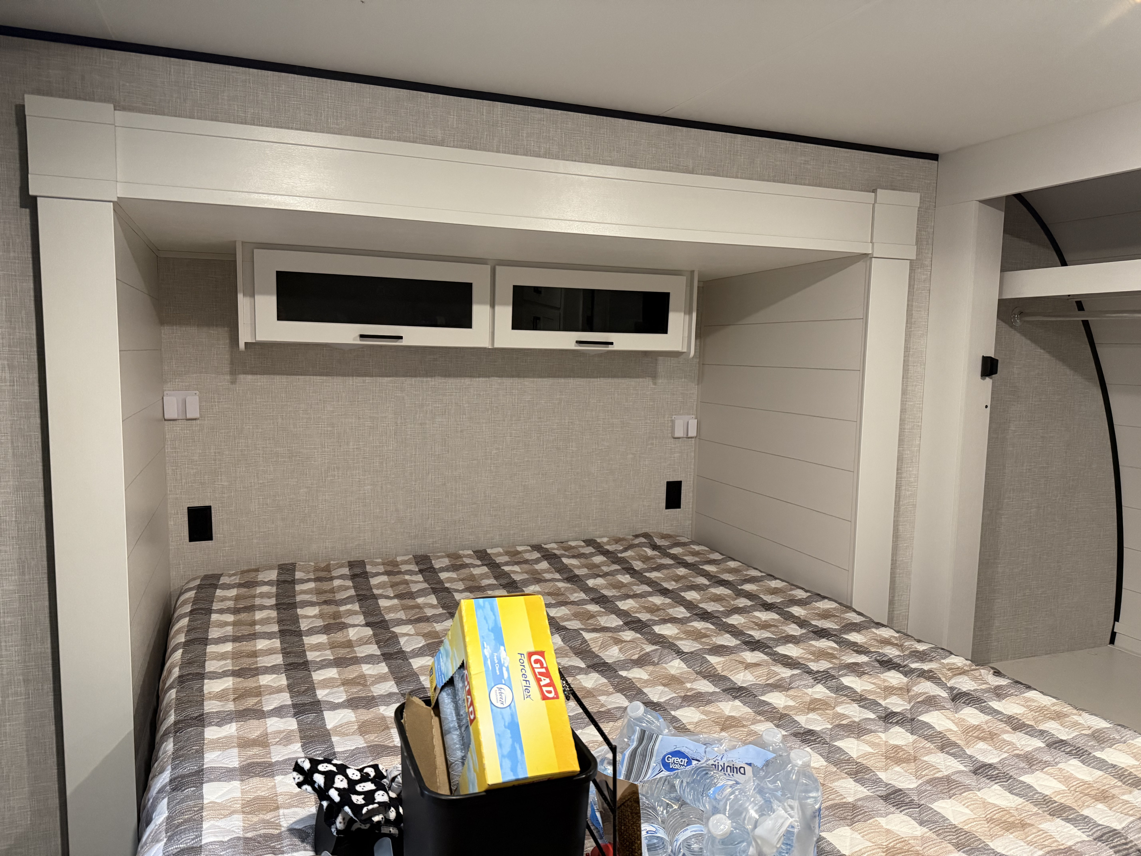 Cozy RV rental bedroom featuring a checkered bed, overhead cabinets, built-in headboard with outlets, and a side closet.. Jayco Jay Flight SLX 2025