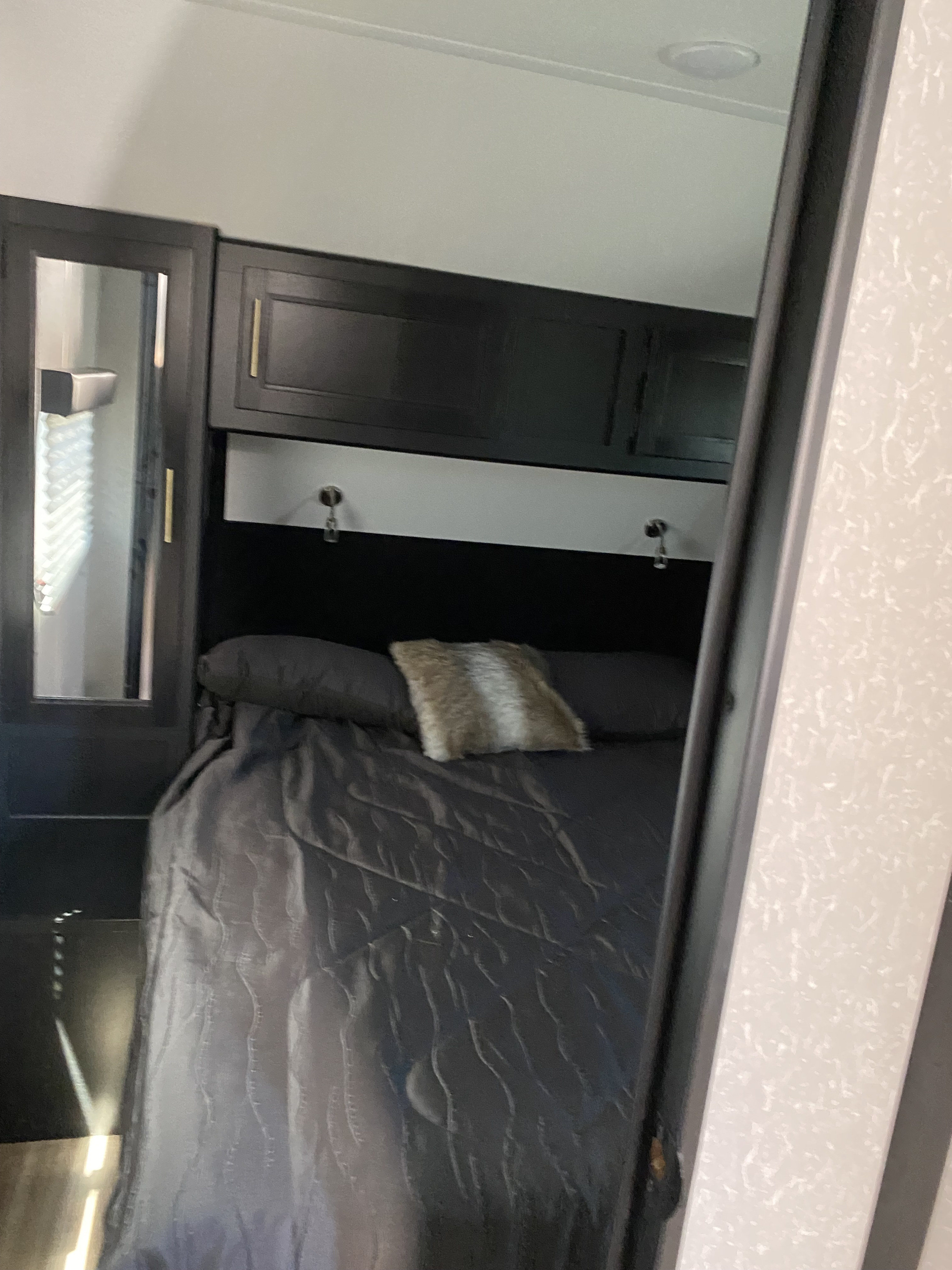 This cozy RV rental bedroom features a comfy bed with dark gray bedding, overhead cabinets, and a mirrored closet.. Forest River Cherokee Grey Wolf 2022