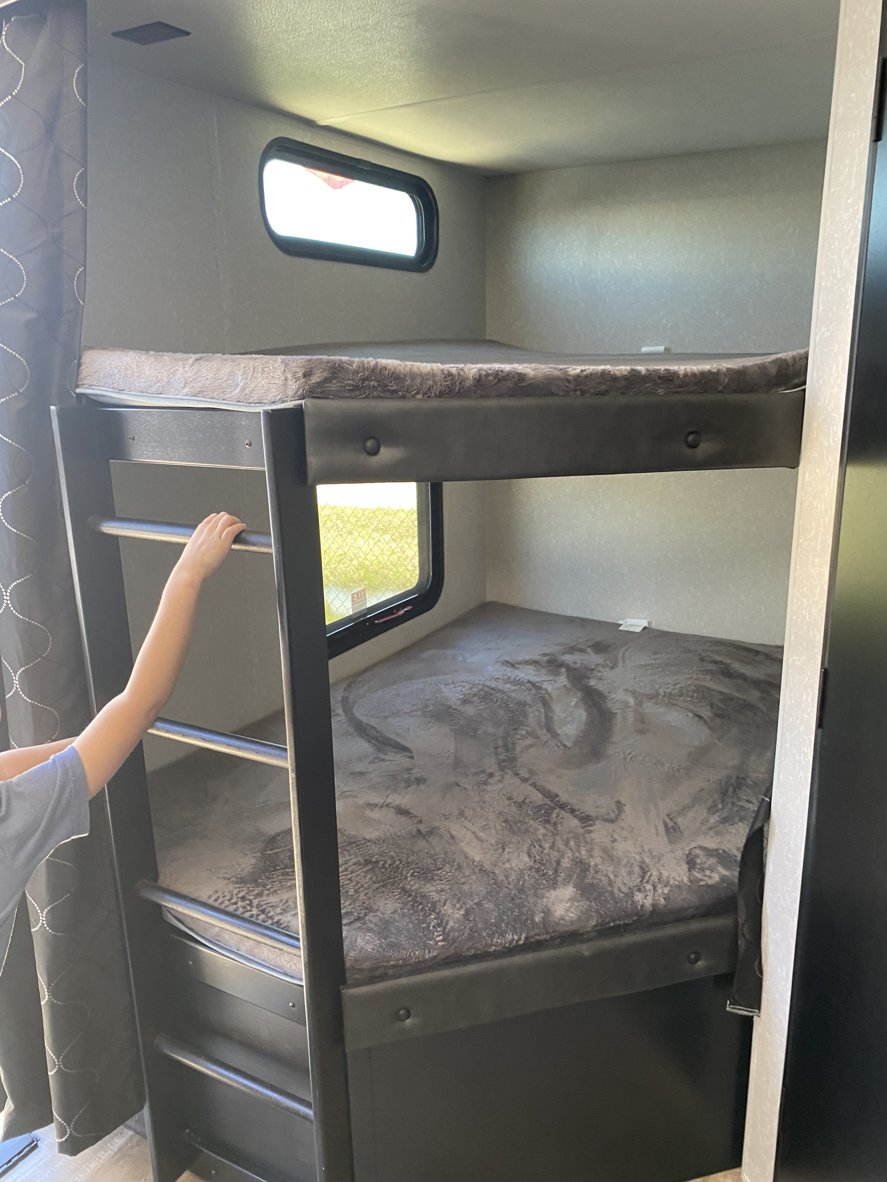 Cozy RV rental bunk beds with windows, perfect for family travel. A child's arm is seen on the ladder to the top bunk.. Forest River Cherokee Grey Wolf 2022