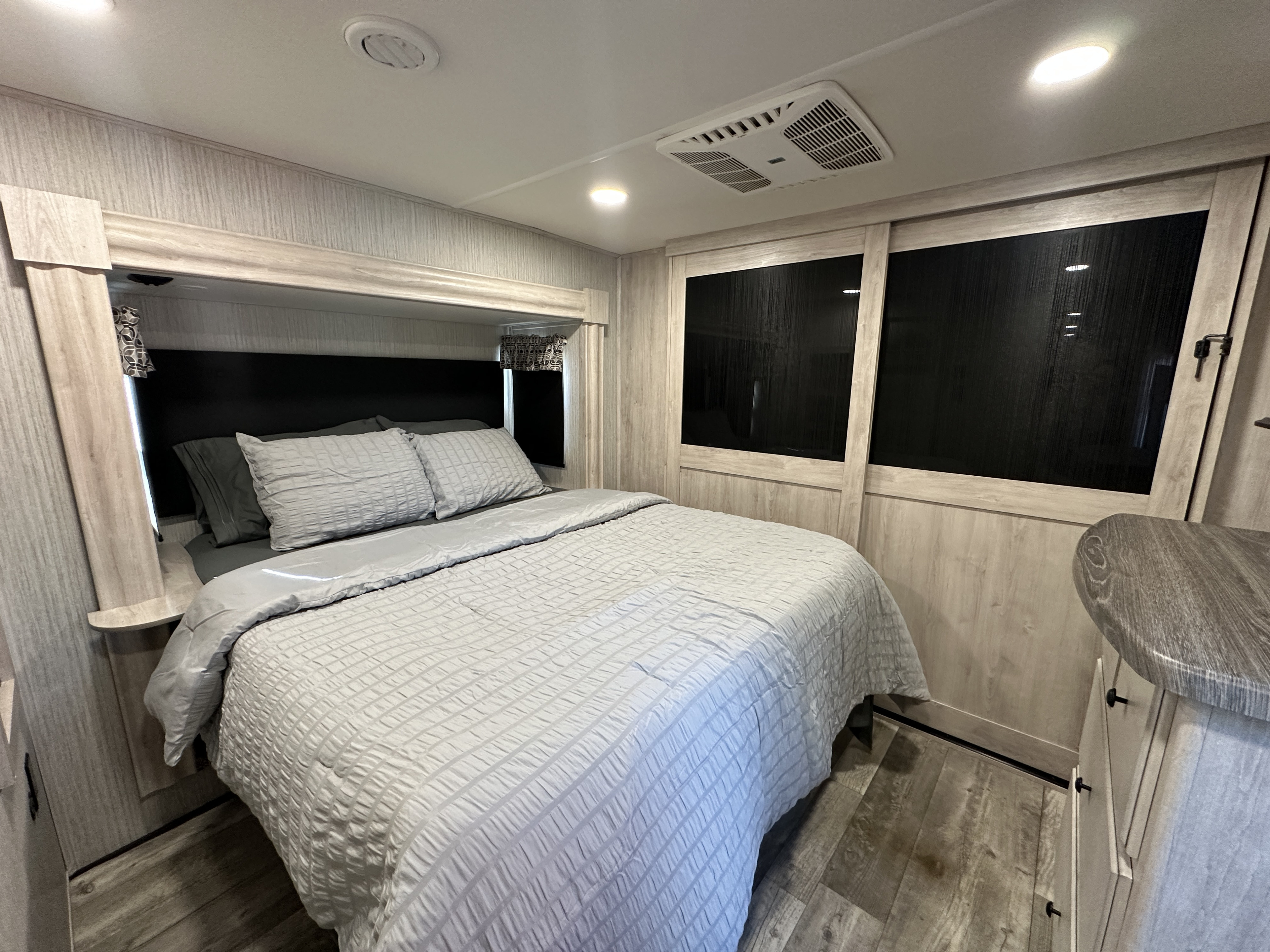 Relaxing RV rental bedroom showcasing a comfortable bed with light gray bedding, light wood interior, and built-in AC.. Forest River Sandpiper 2022