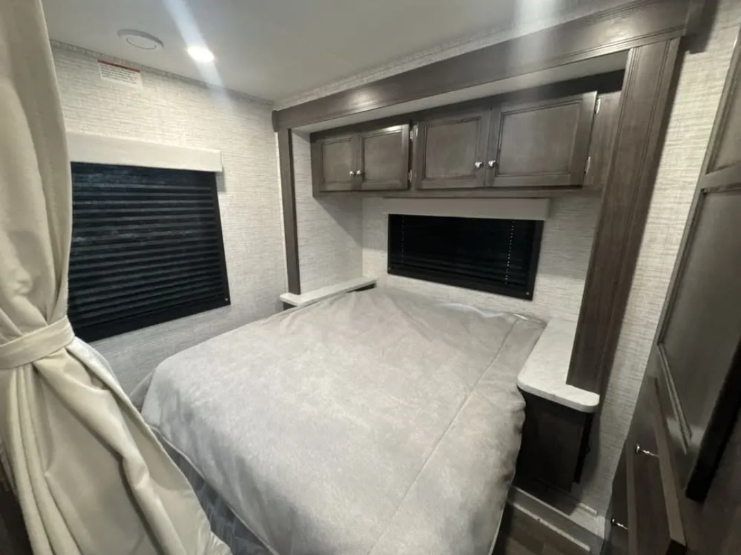 RV rental bedroom featuring a comfortable bed, overhead storage, and windows with blinds. A compact, inviting space.. Jayco Redhawk SE 2025