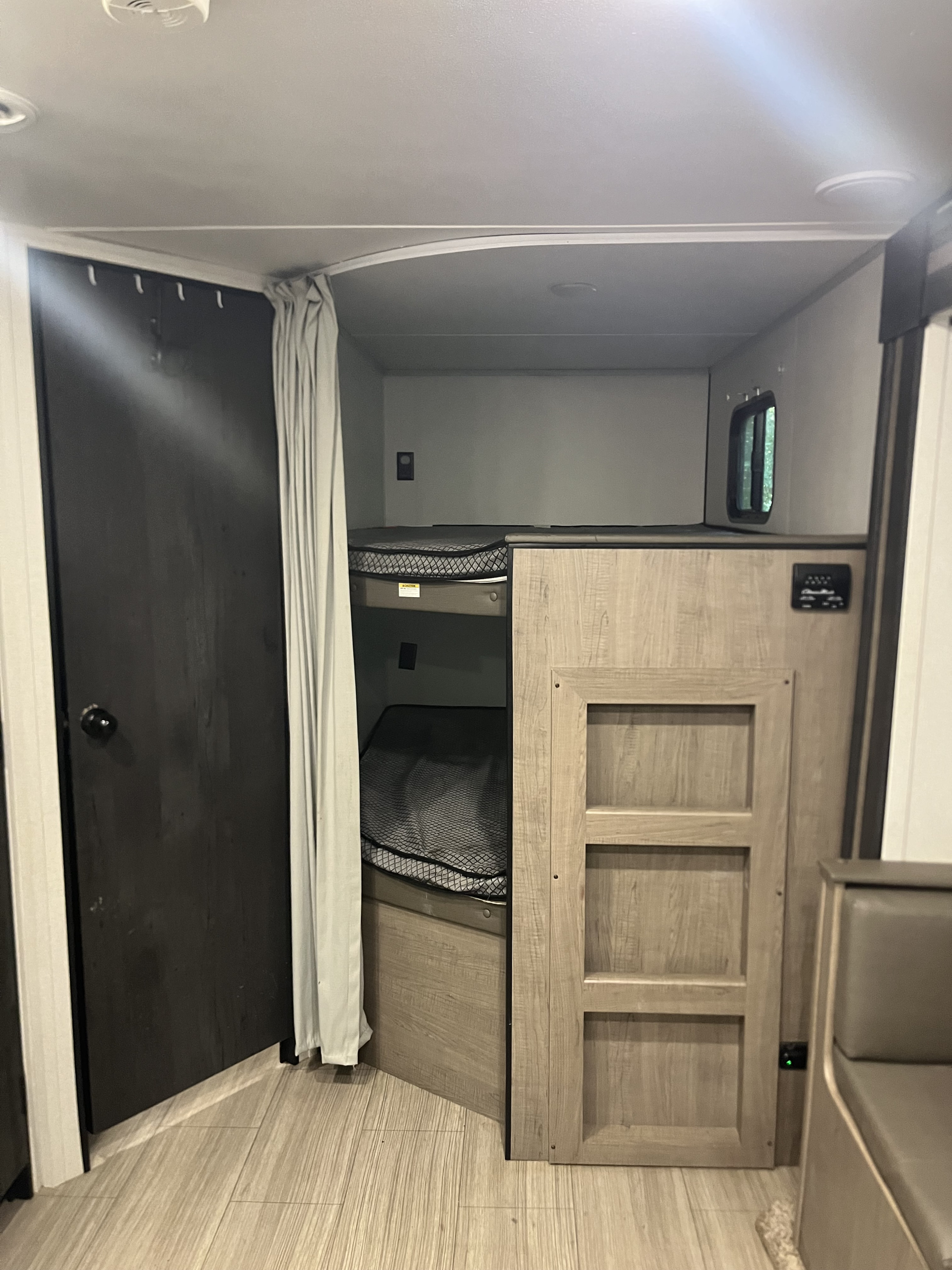 RV rental interior featuring cozy bunk beds with nets, a dark door, privacy curtain, and light wood finishes.. Keystone RV Hideout 2021