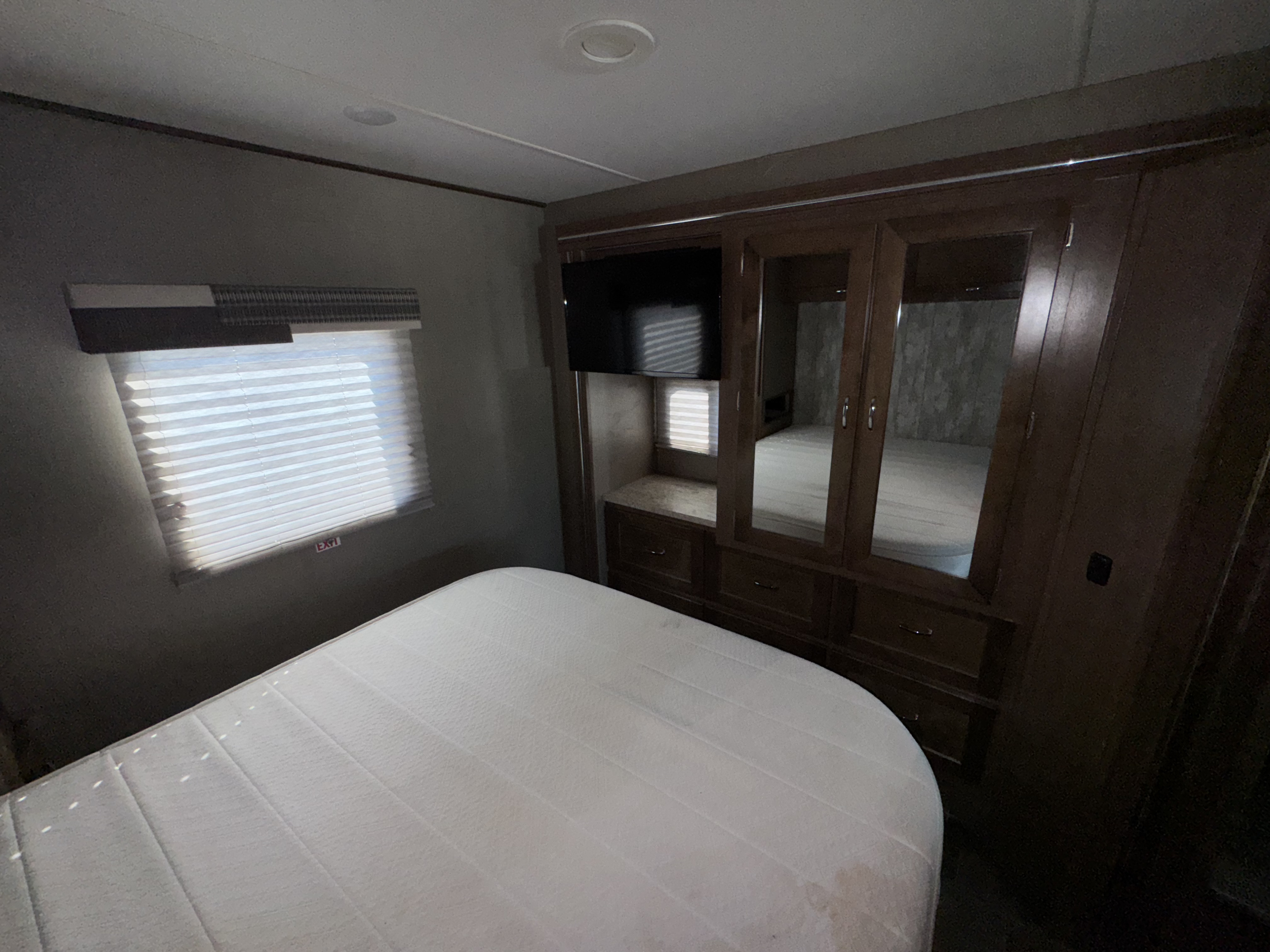 This RV rental bedroom includes a clean white mattress, a mirrored wardrobe, a TV, and a window with blinds.. Winnebago Intent 2018