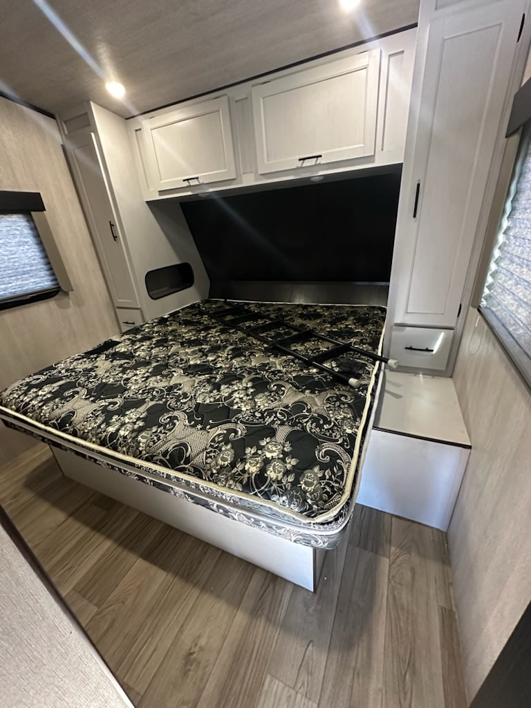 Cozy rv rental bedroom featuring a patterned bed, overhead storage, side wardrobes, and modern wood flooring.. Genesis Supreme Rv Genesis Supreme 2025