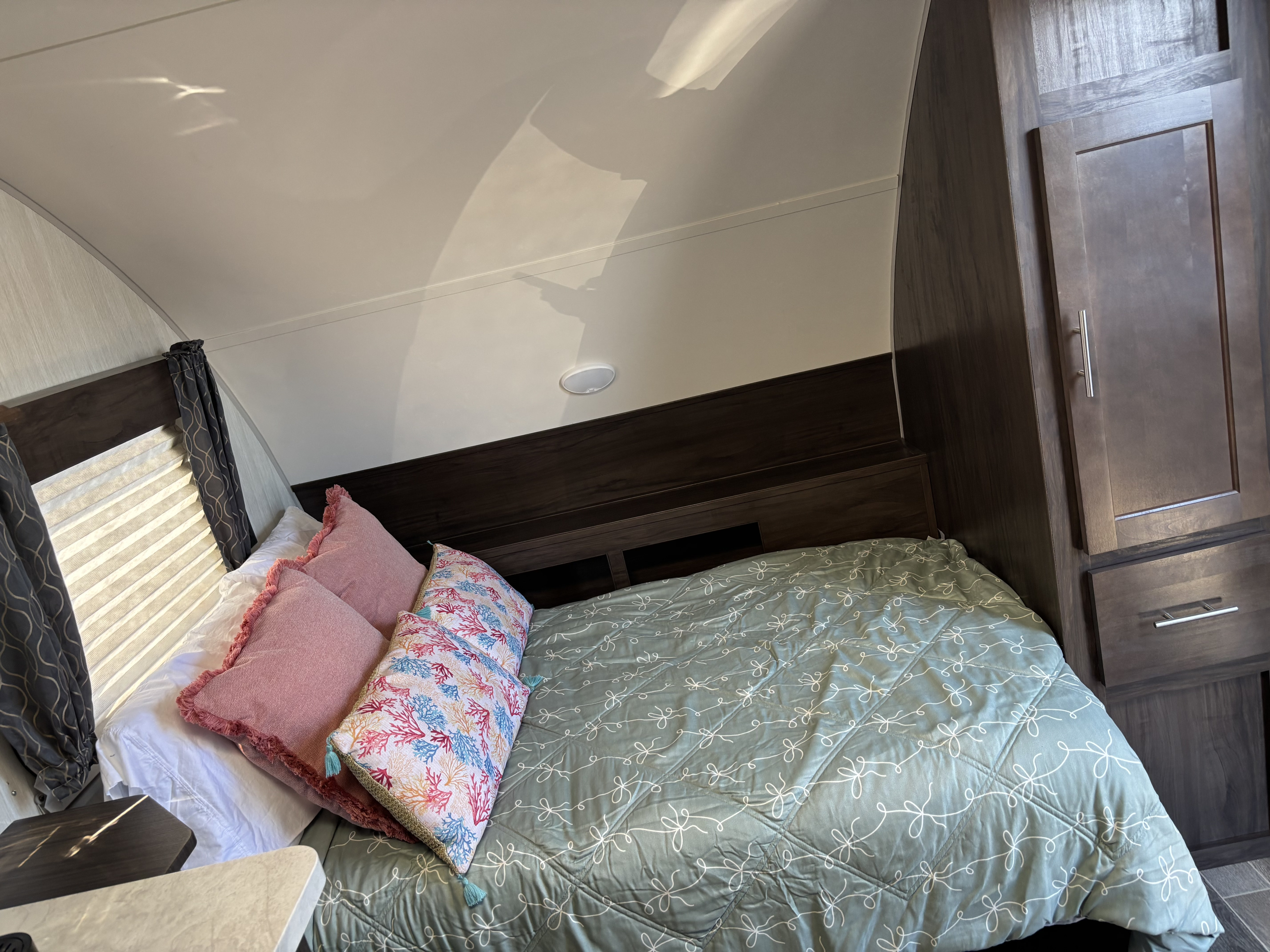 An inviting RV rental bedroom featuring a bed with a green patterned comforter, vibrant pillows, and wooden storage.. Forest River Cherokee 2019