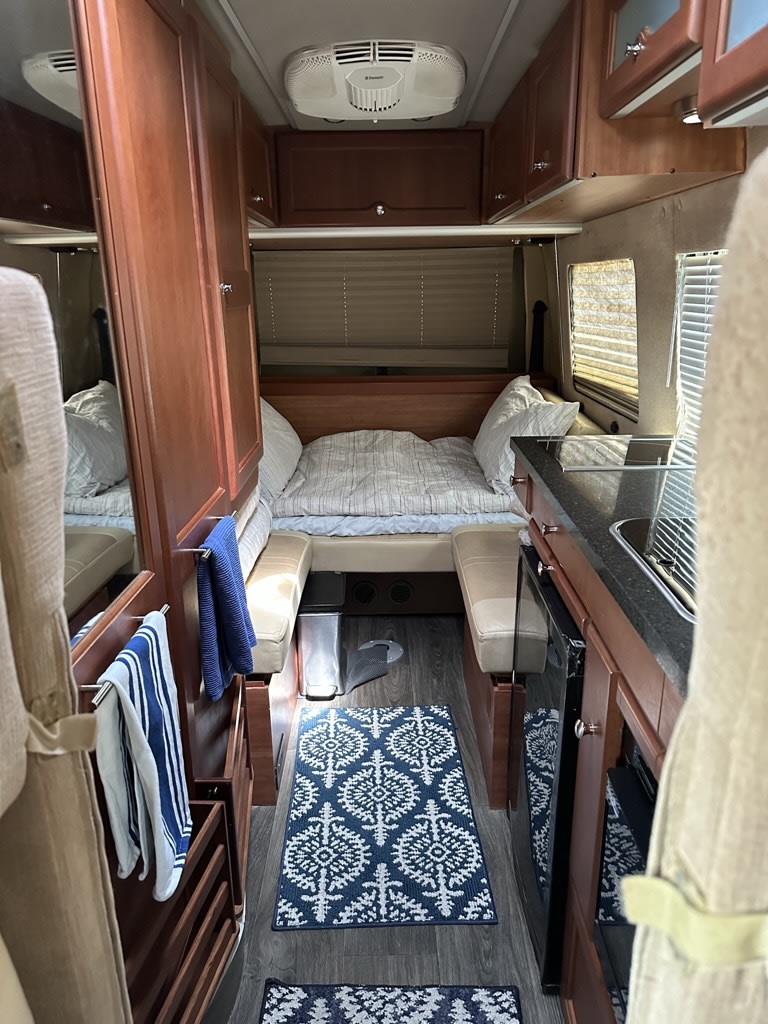 Inside a well-appointed rv rental: rear bed, compact kitchen with sink, wood cabinets, and patterned rug. Cozy travel space.. Roadtrek RS Adventurous XL 2017