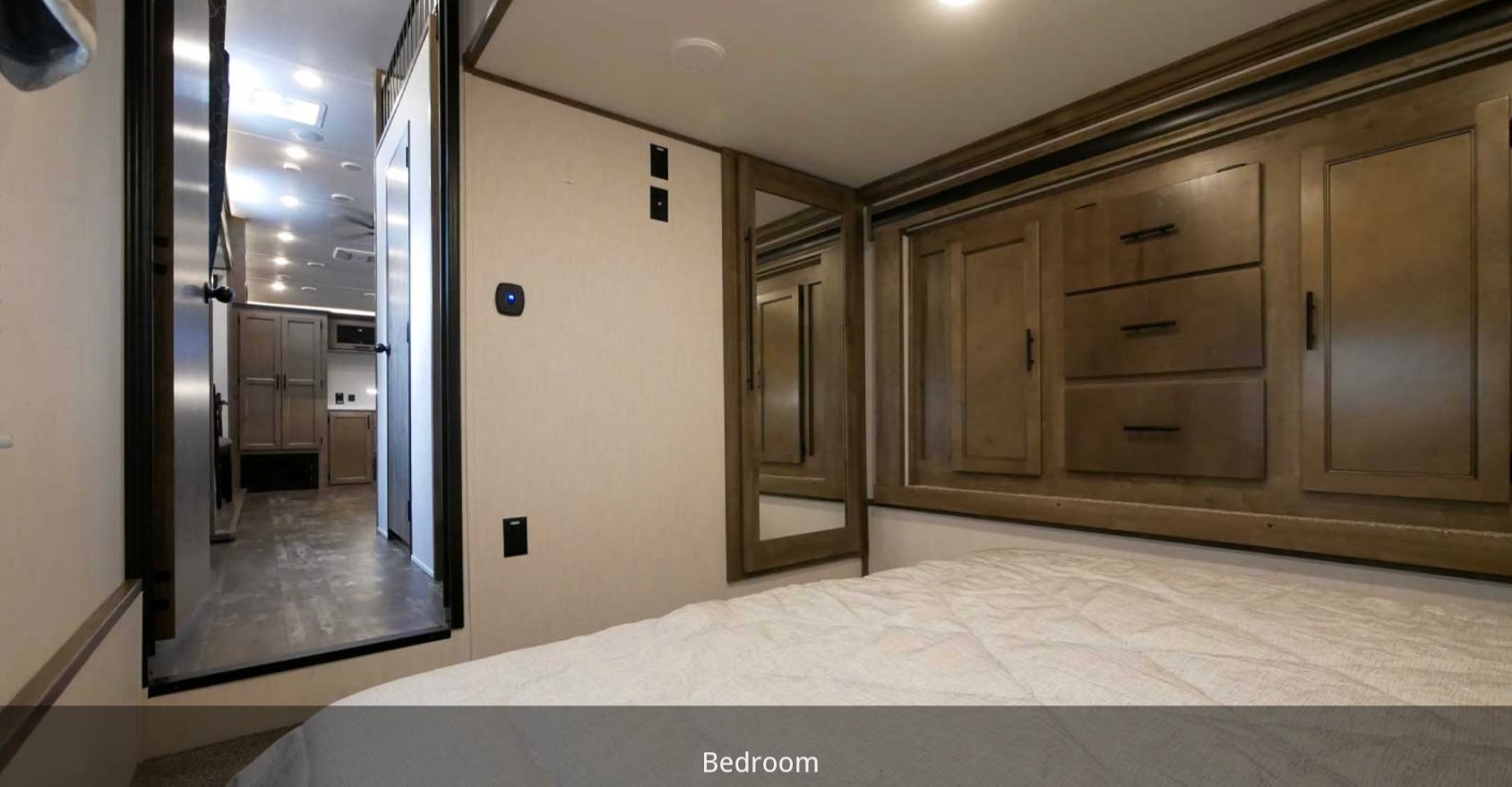 RV rental bedroom with a bed, wood cabinetry, mirror, and a glimpse into the RV's hallway and living area.. Forest River Sabre 2021