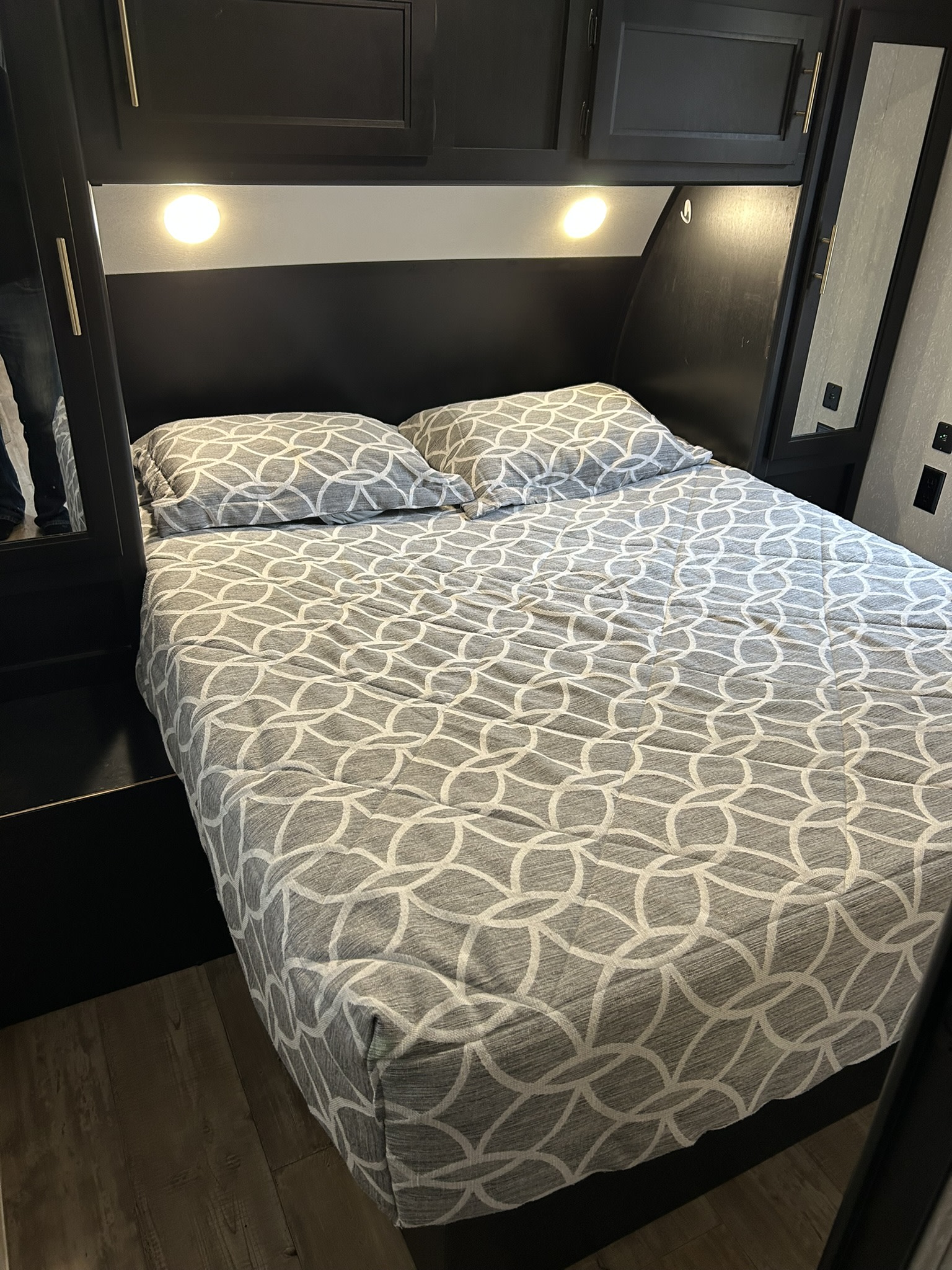 Cozy RV rental bedroom with a gray patterned bed, dark overhead cabinets, and built-in lights for comfortable travel.. Forest River Cherokee 2021