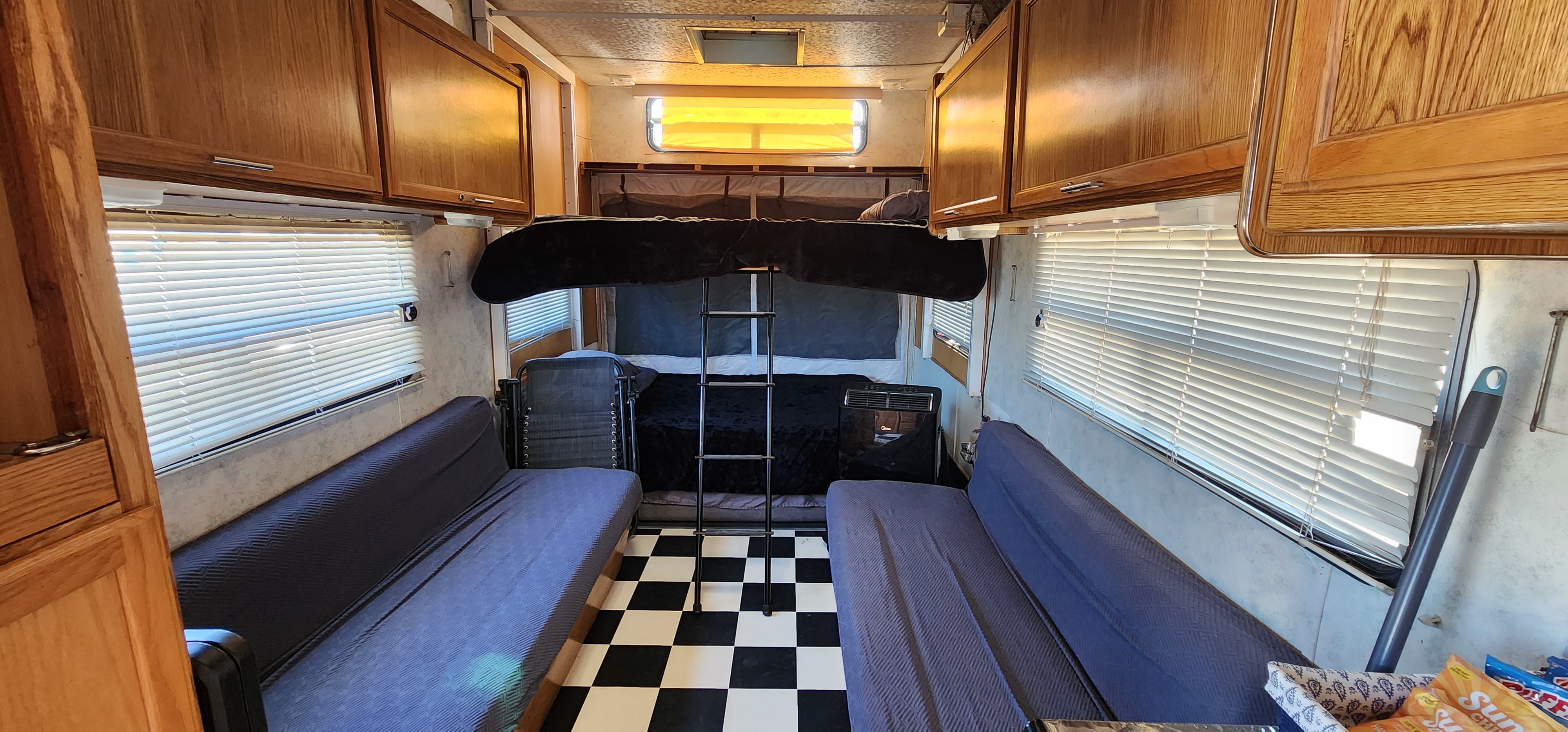 RV rental interior featuring a checkered floor, side futon seating, and a bunk bed with a ladder, offering a compact living space.. Forest River Salem 2000