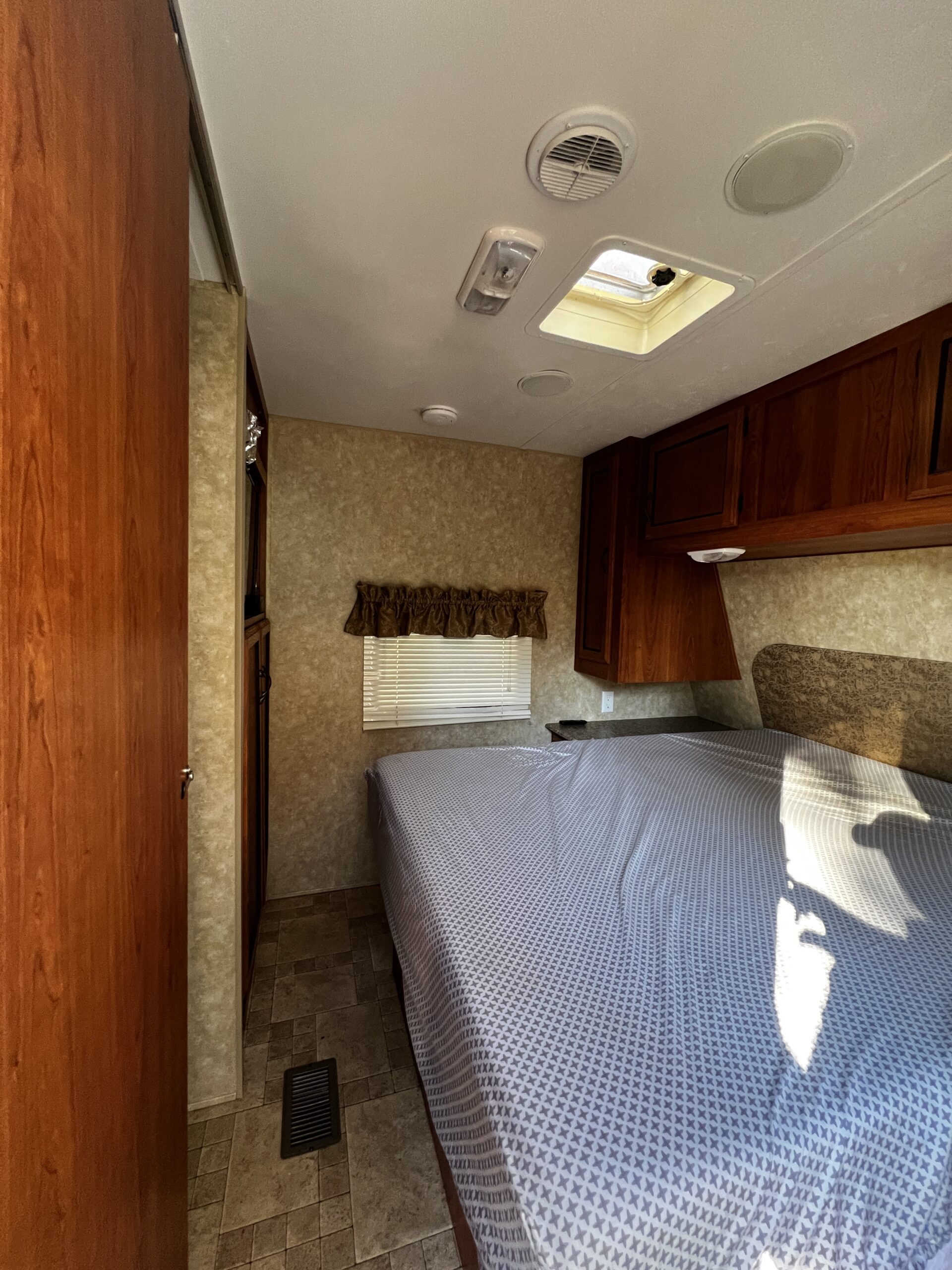 Cozy RV rental bedroom featuring a comfortable bed, wood cabinets, skylight, and window blinds. Perfect for travel accommodation.. Coachman Catalina 2012