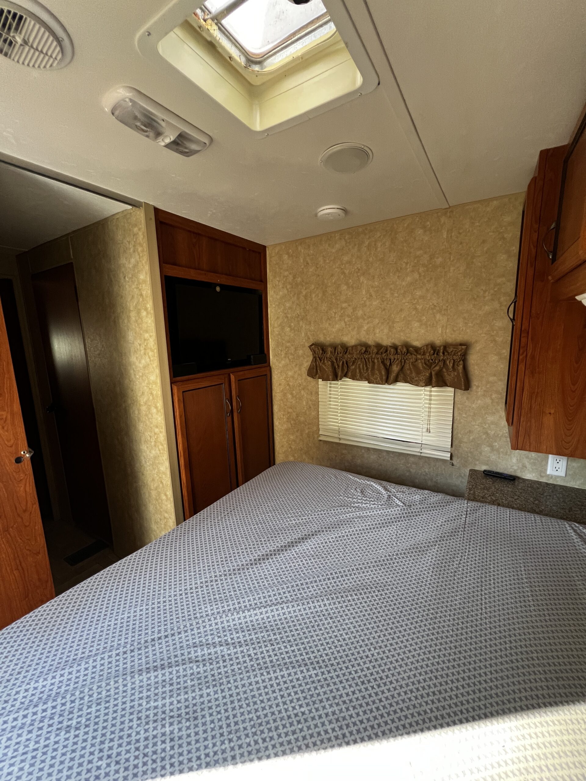 RV rental bedroom: patterned bed, TV, window with blinds, ceiling vent, skylight, and lights. Ready for your adventure.. Coachman Catalina 2012