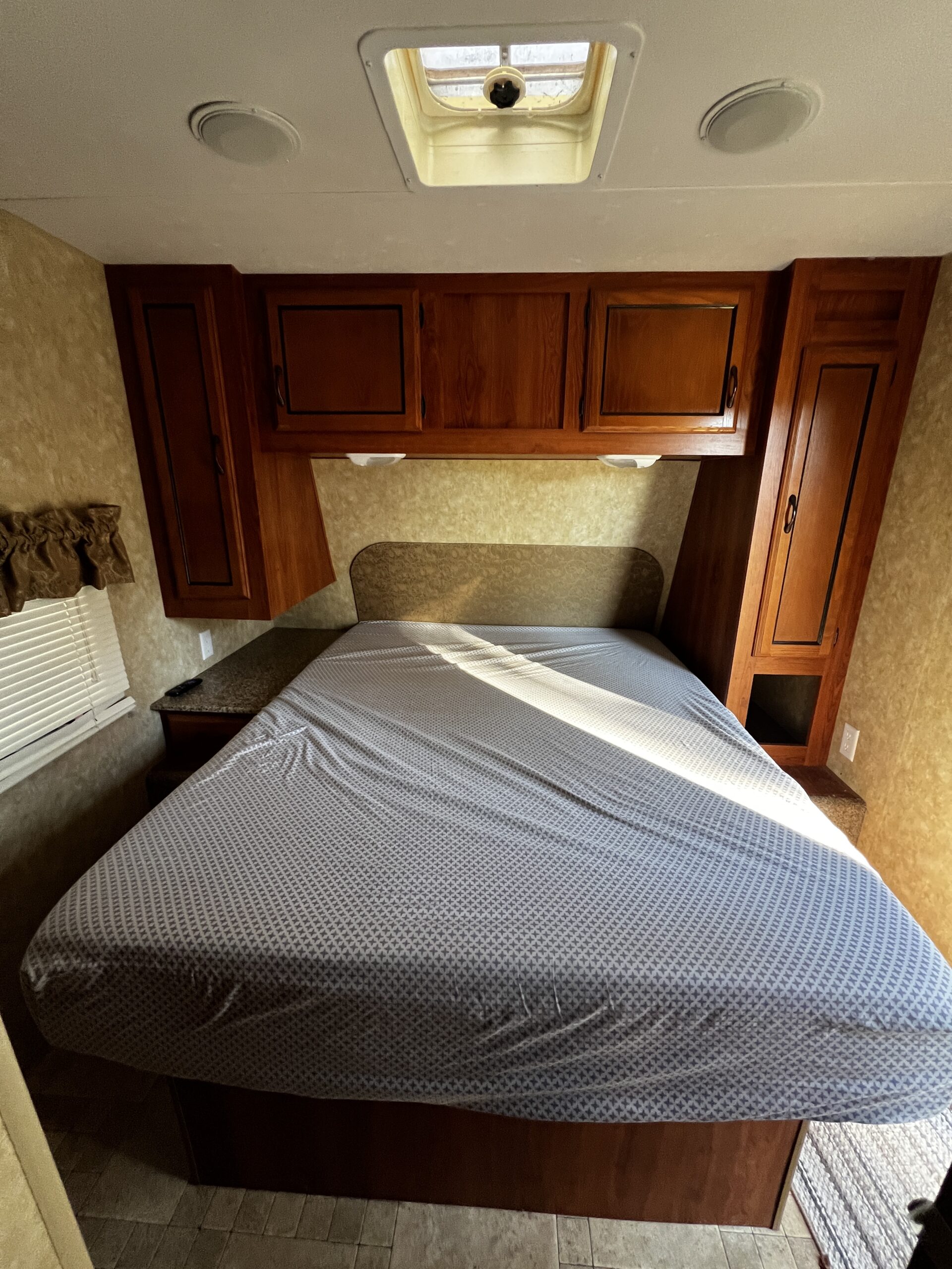 Experience comfort in this RV rental bedroom with a bed, overhead wooden cabinets, ceiling speakers, and a skylight.. Coachman Catalina 2012