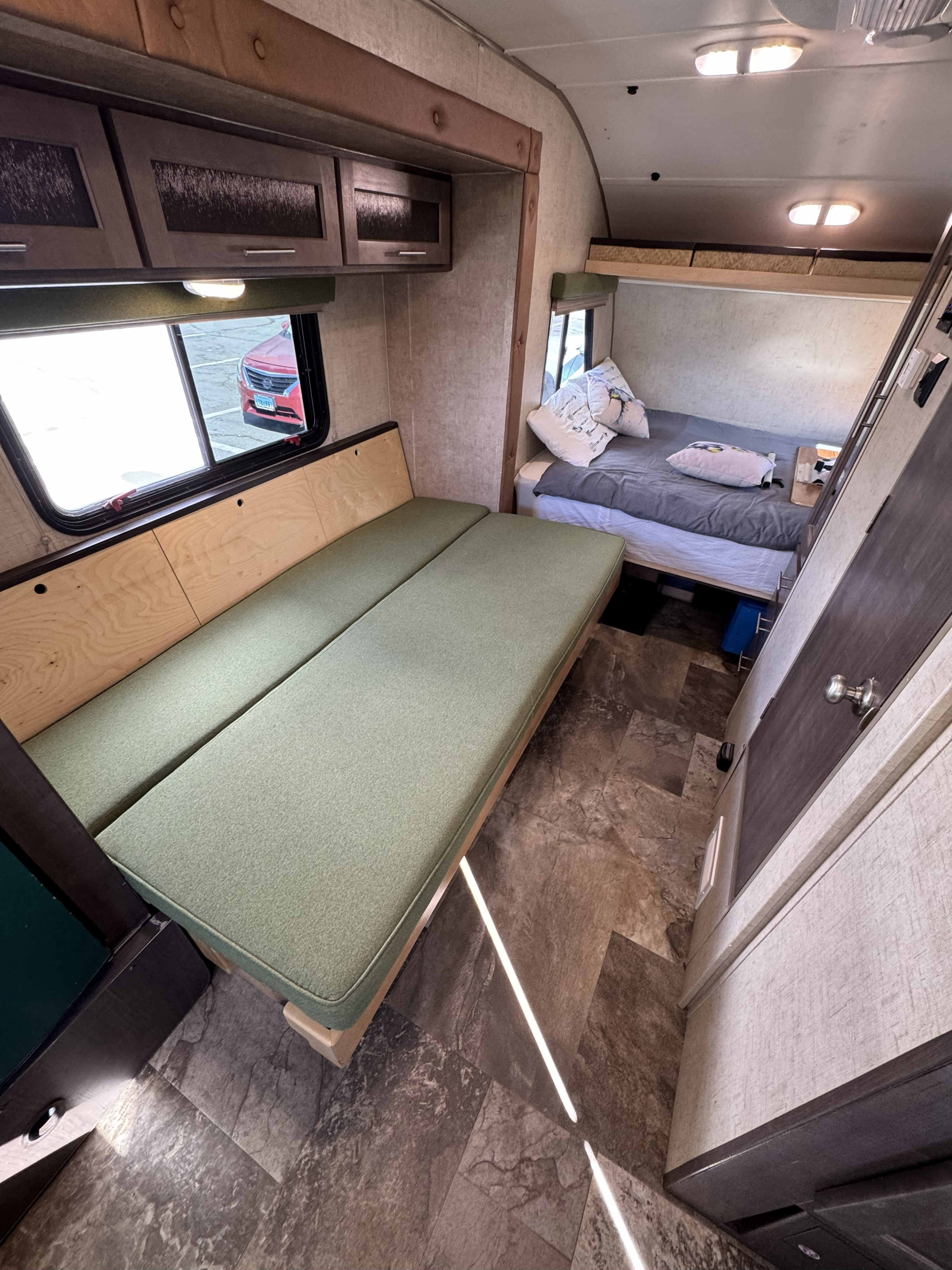 Interior view of an RV rental: green bench seating, overhead cabinets, a cozy bed, and a window view.. R-Pod Hood River Edition 2015