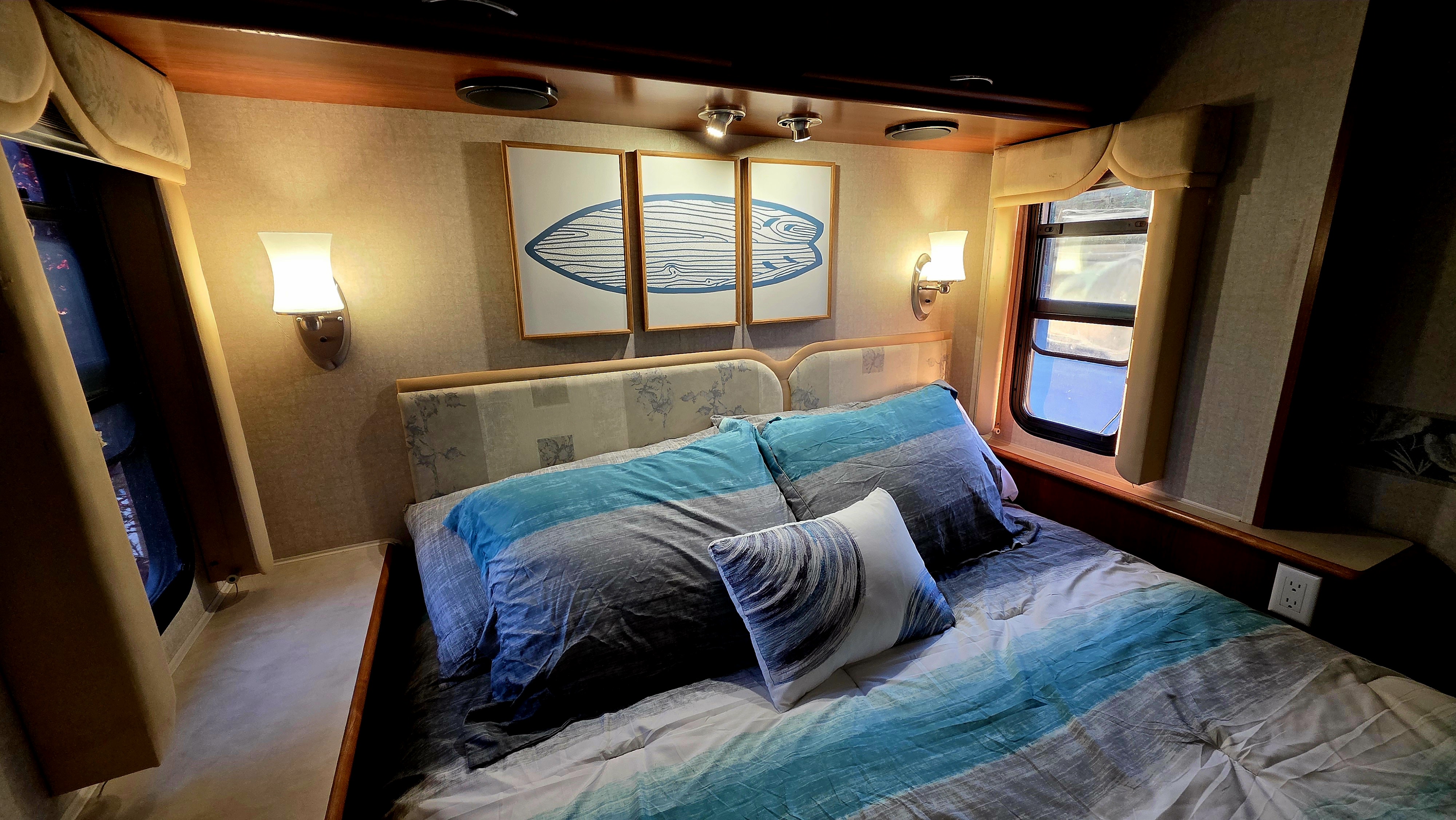A cozy RV rental bedroom features blue and gray bedding, warm lighting, and surf-themed wall art, ready for your next trip.. Fleetwood Southwind Motorhome 2007