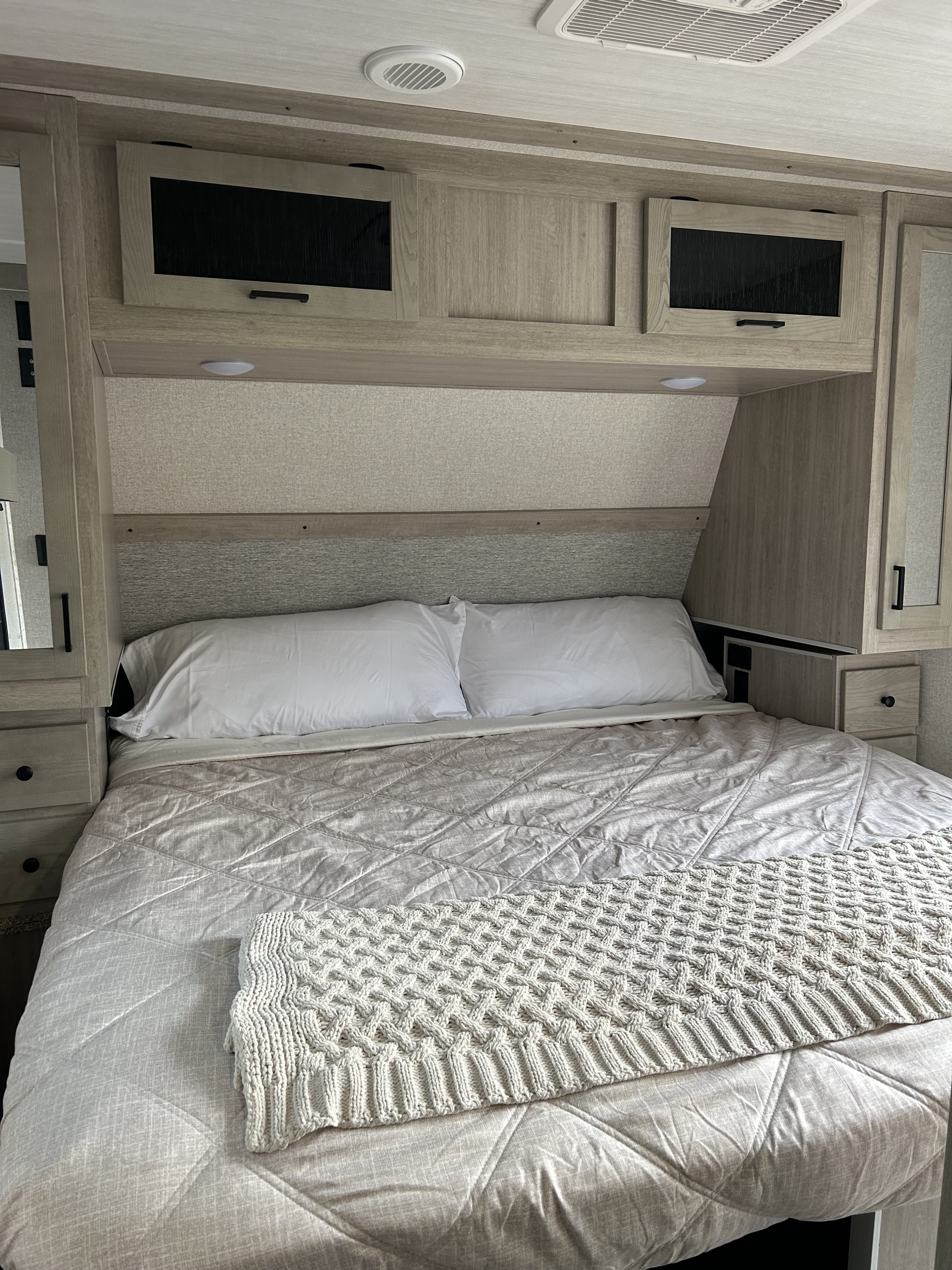 This RV rental bedroom offers a comfortable bed with a quilted comforter, white pillows, and practical overhead storage.. East to West Alta 2023