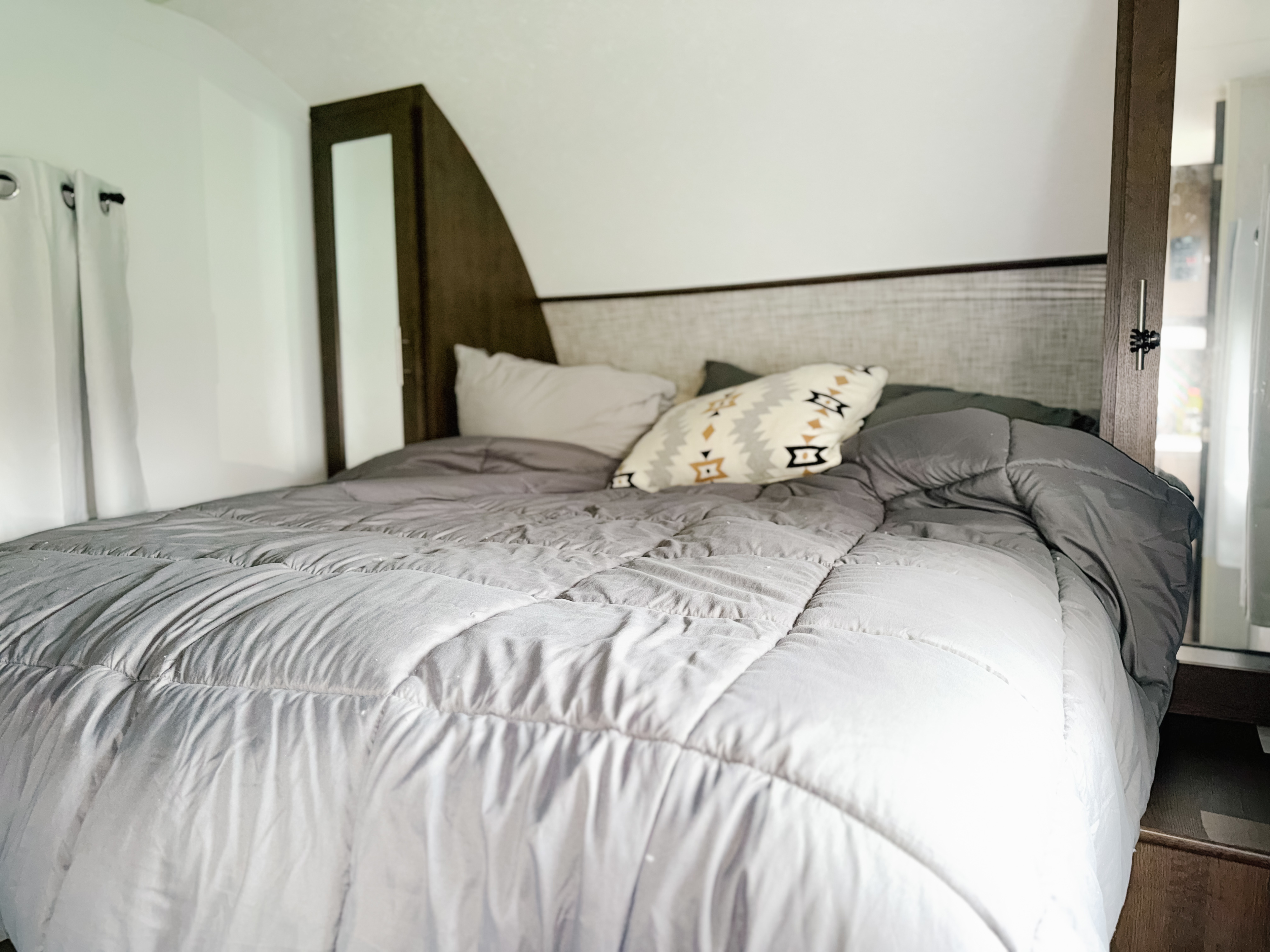 Comfortable RV rental bedroom featuring a made bed with a gray comforter, white & patterned pillows, and white curtains.. Forest River Salem 2019