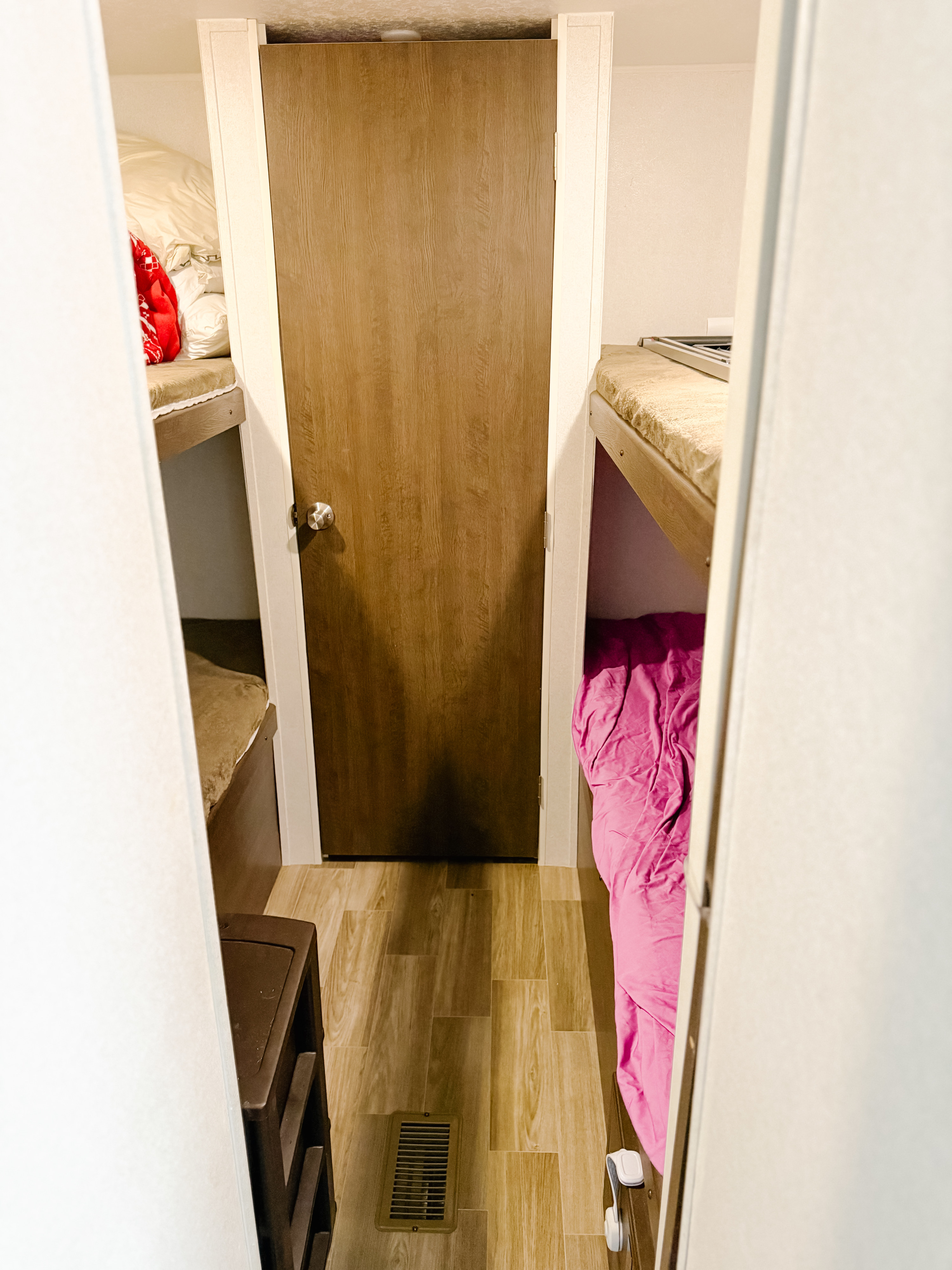 Inside an RV rental: a narrow bunk bed hallway with beds on each side and a closed wooden door ahead.. Forest River Salem 2019