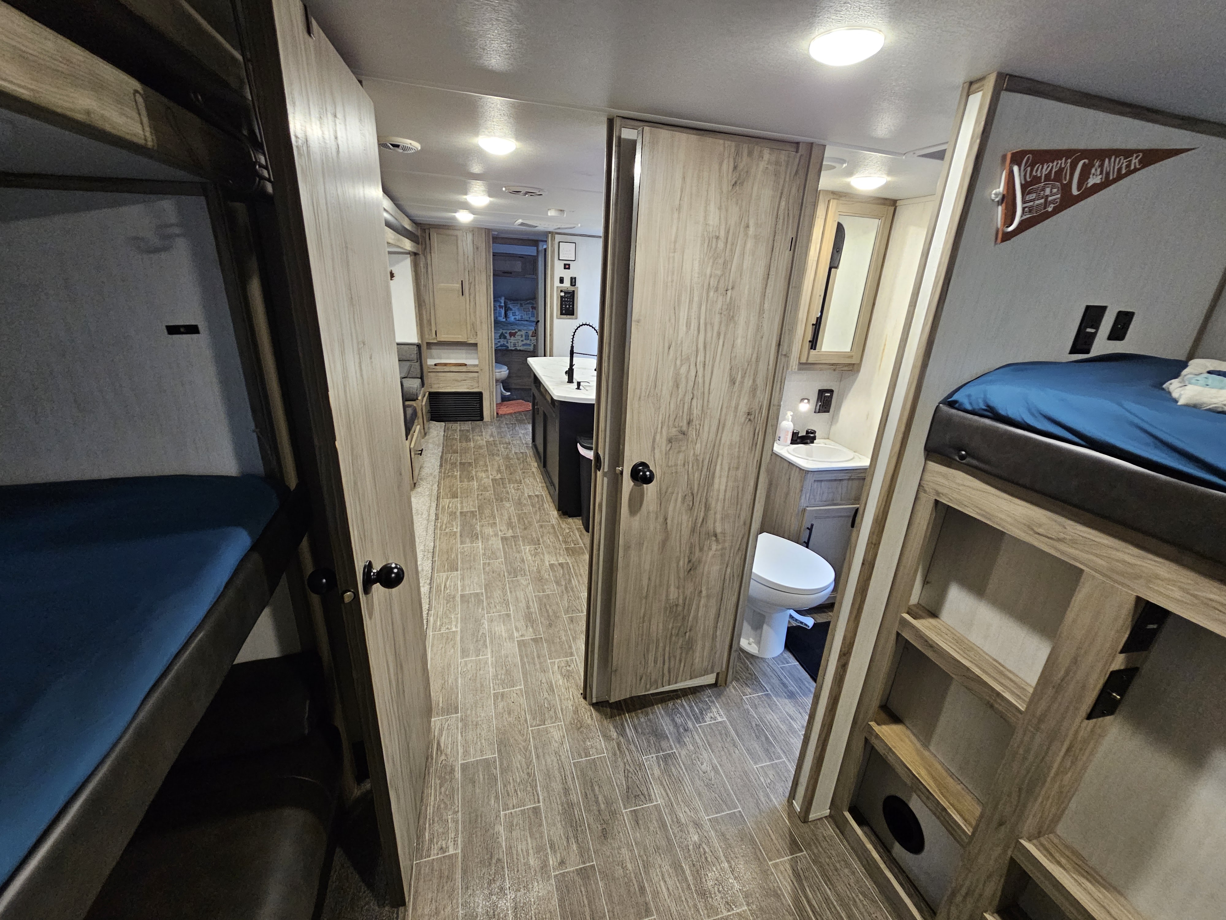 Spacious rv rental interior featuring bunk beds, a central hallway leading to a kitchen, and a visible bathroom on the right.. Forest River Cherokee Alpha Wolf 2021