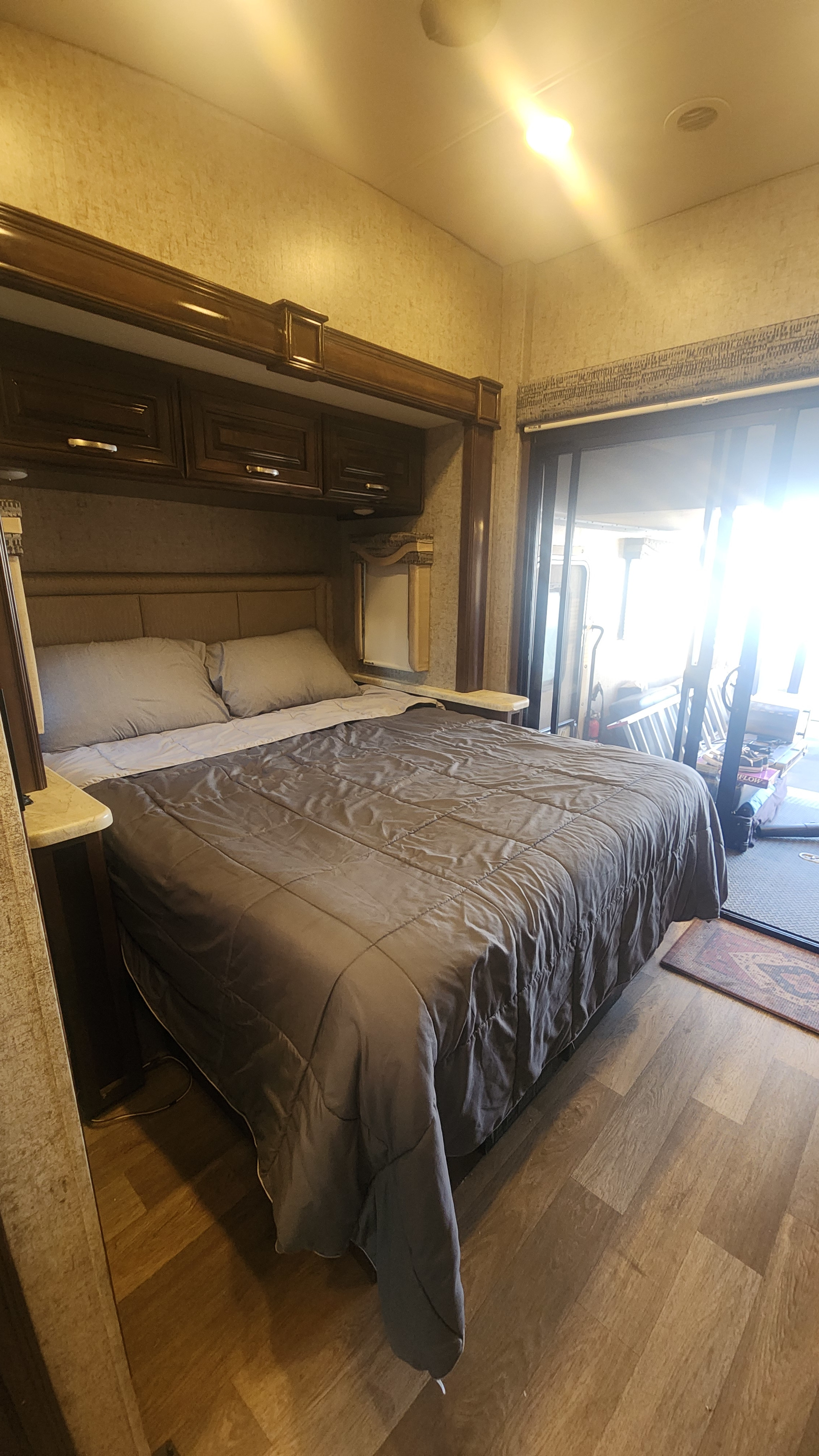 Comfortable RV rental bedroom with dark wood cabinets, a large bed, and bright natural light from a sliding door.. Thor Outlaw 2017