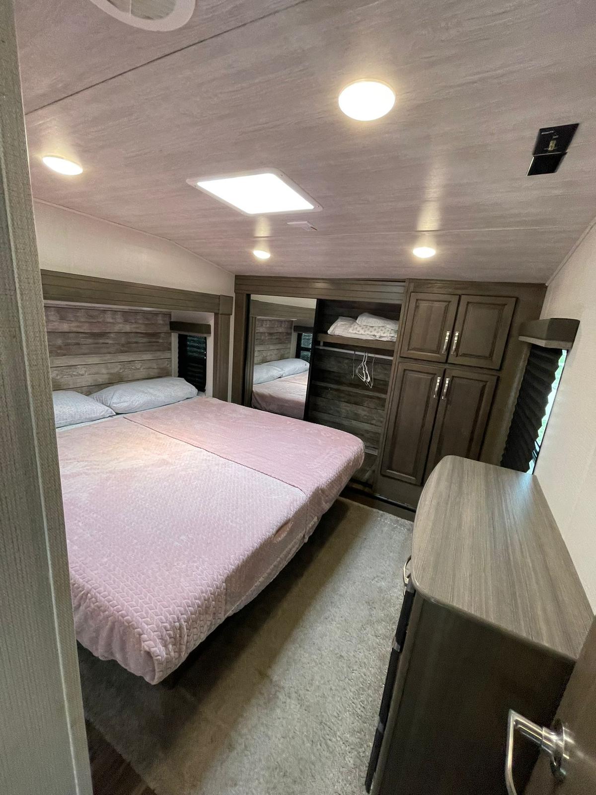 Cozy RV rental bedroom with a pink bed, mirrored closet, & dresser. Perfect for your travel trailer getaway.. COUGAR 316RLS 2021