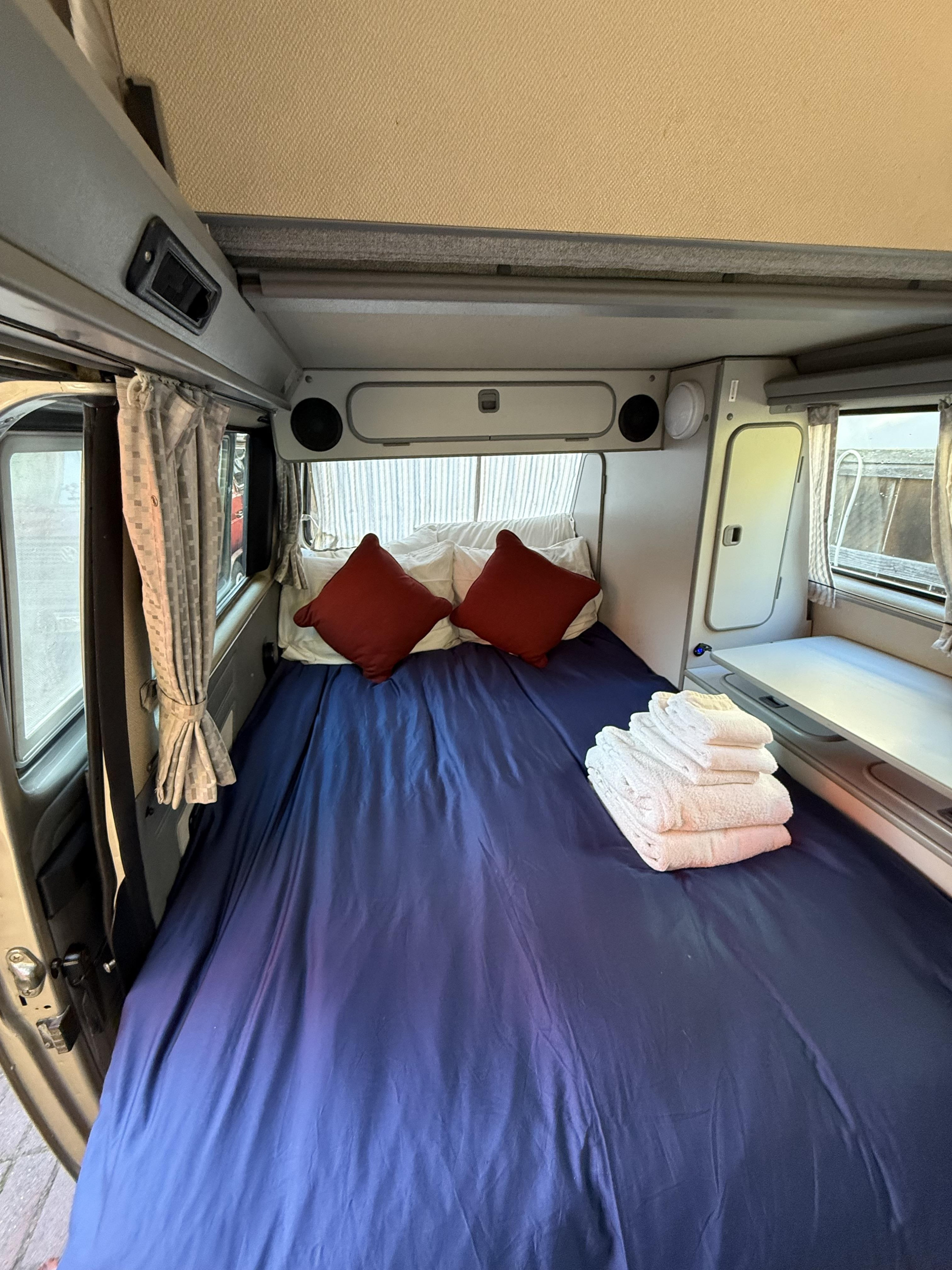 Cozy campervan bed setup for your next rv rental adventure, complete with fresh towels and red pillows.. Volkswagen T3 Westfalia 1991