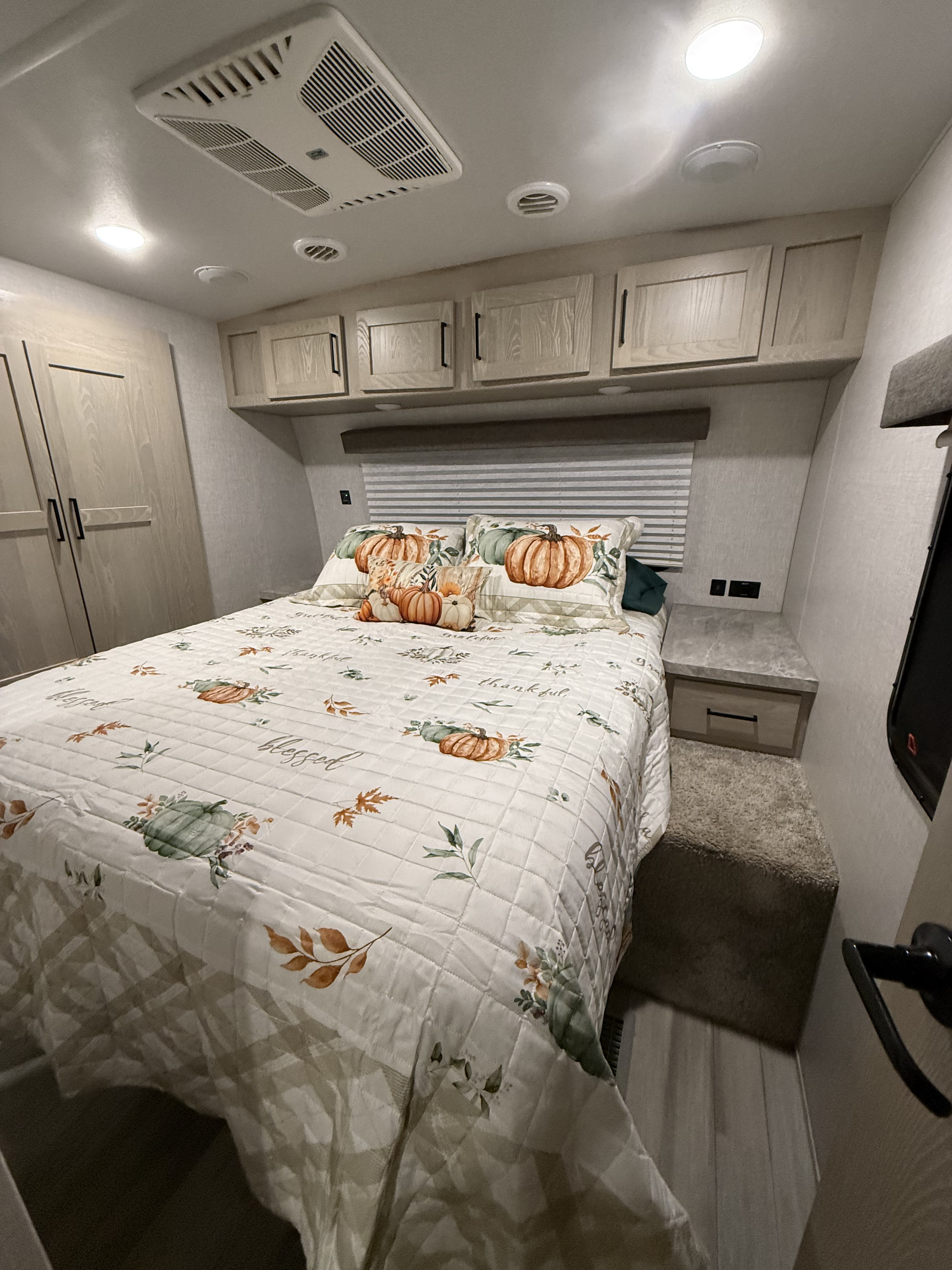 Cozy RV rental bedroom features autumn-themed bedding, overhead cabinets, and climate control for comfortable travels.. Forest River Rockwood Ultra Lite 2021