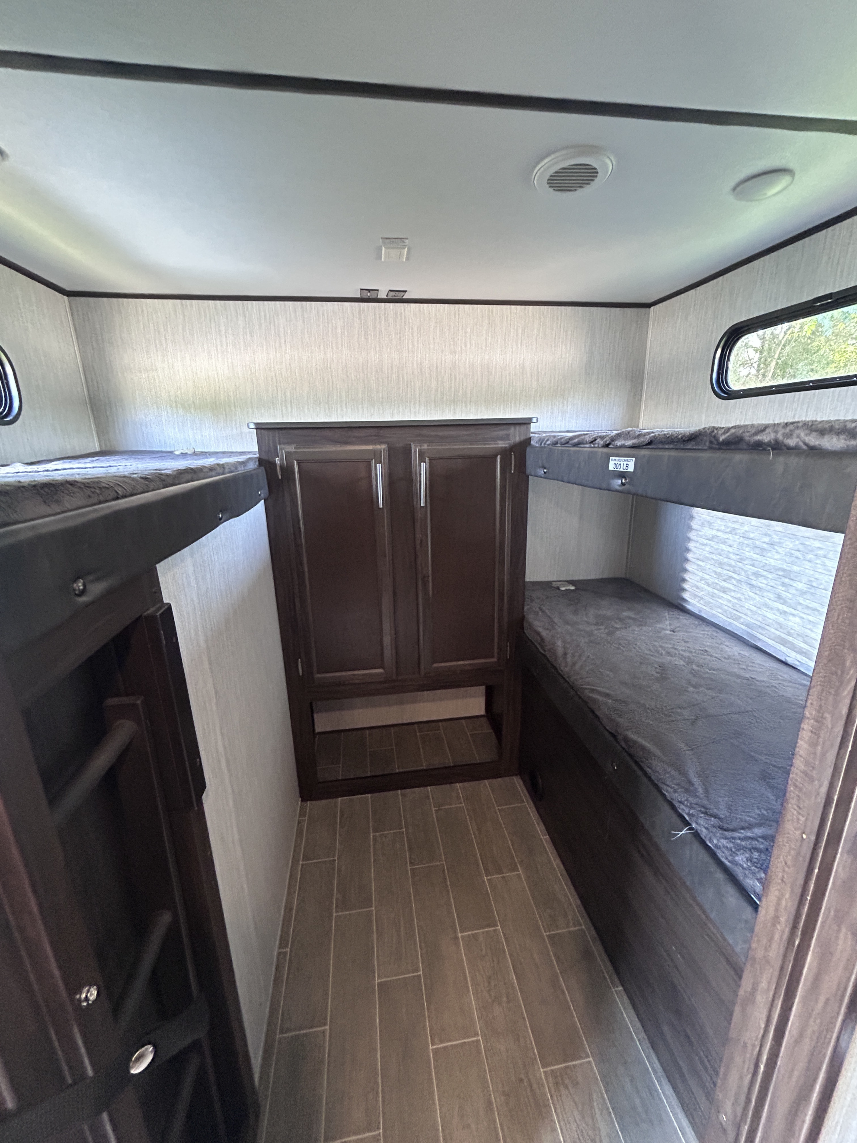 Inside this RV rental, find two bunk beds with cozy blankets, a central cabinet, and modern wood-look tile flooring.. Escape Trailer Alpha Wolf 2020