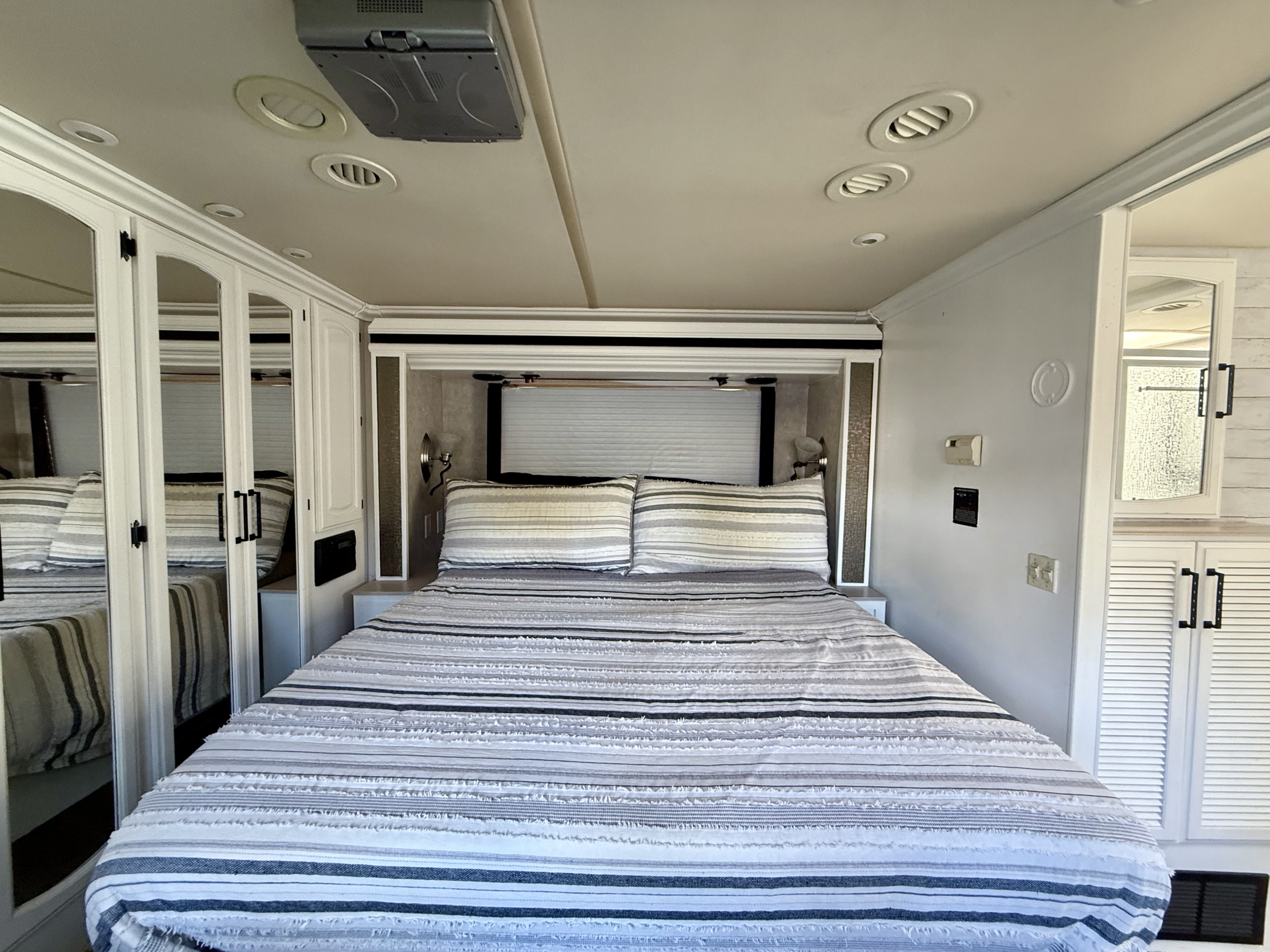 A cozy RV rental bedroom interior with a queen-sized bed, striped bedding, mirrored wardrobes, and recessed lighting for travel comfort.. Fleetwood Providence 2003
