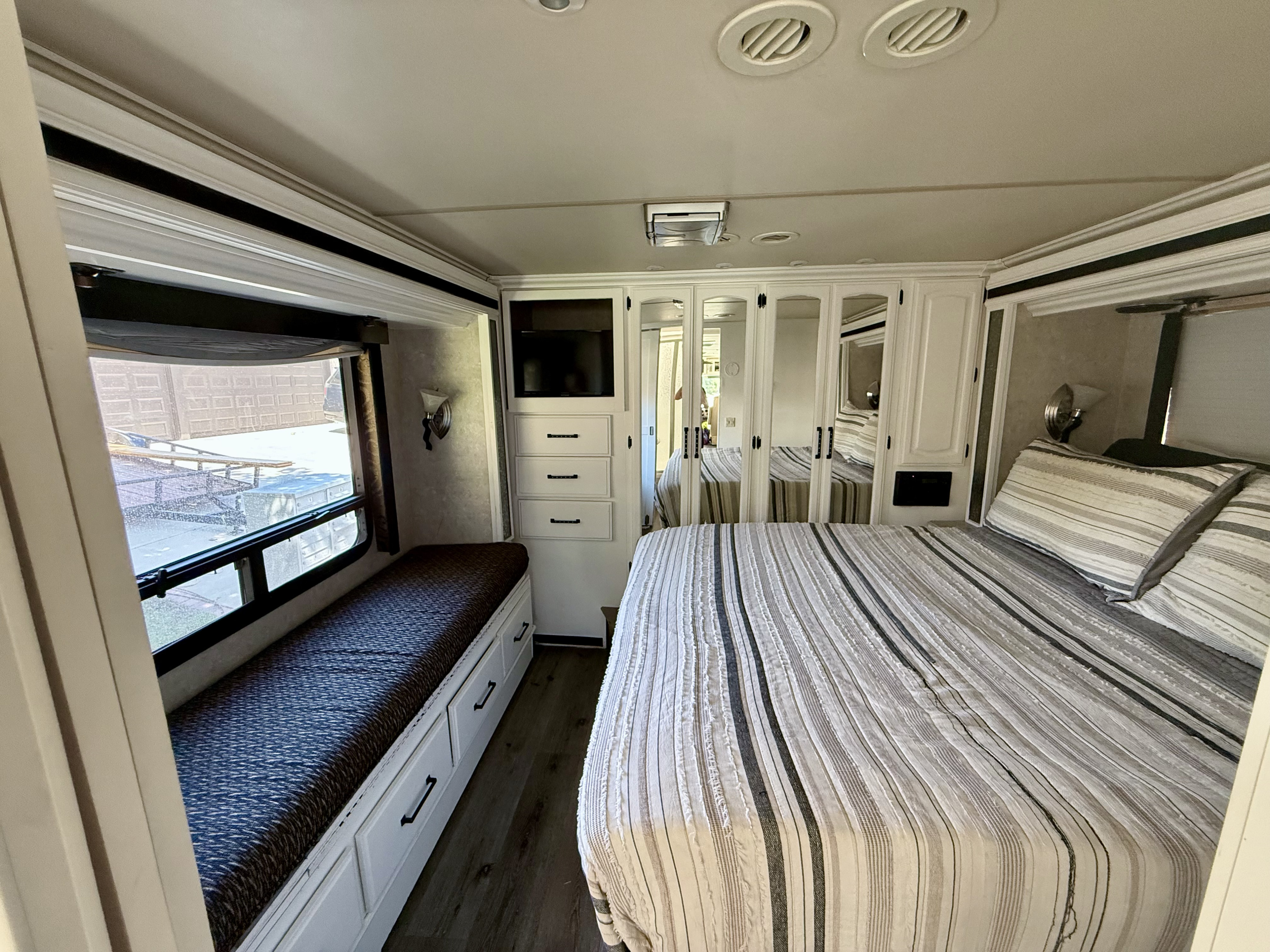 Cozy RV rental bedroom with a striped bed, window-side bench, storage, TV, and mirrored closets for your journey.. Fleetwood Providence 2003