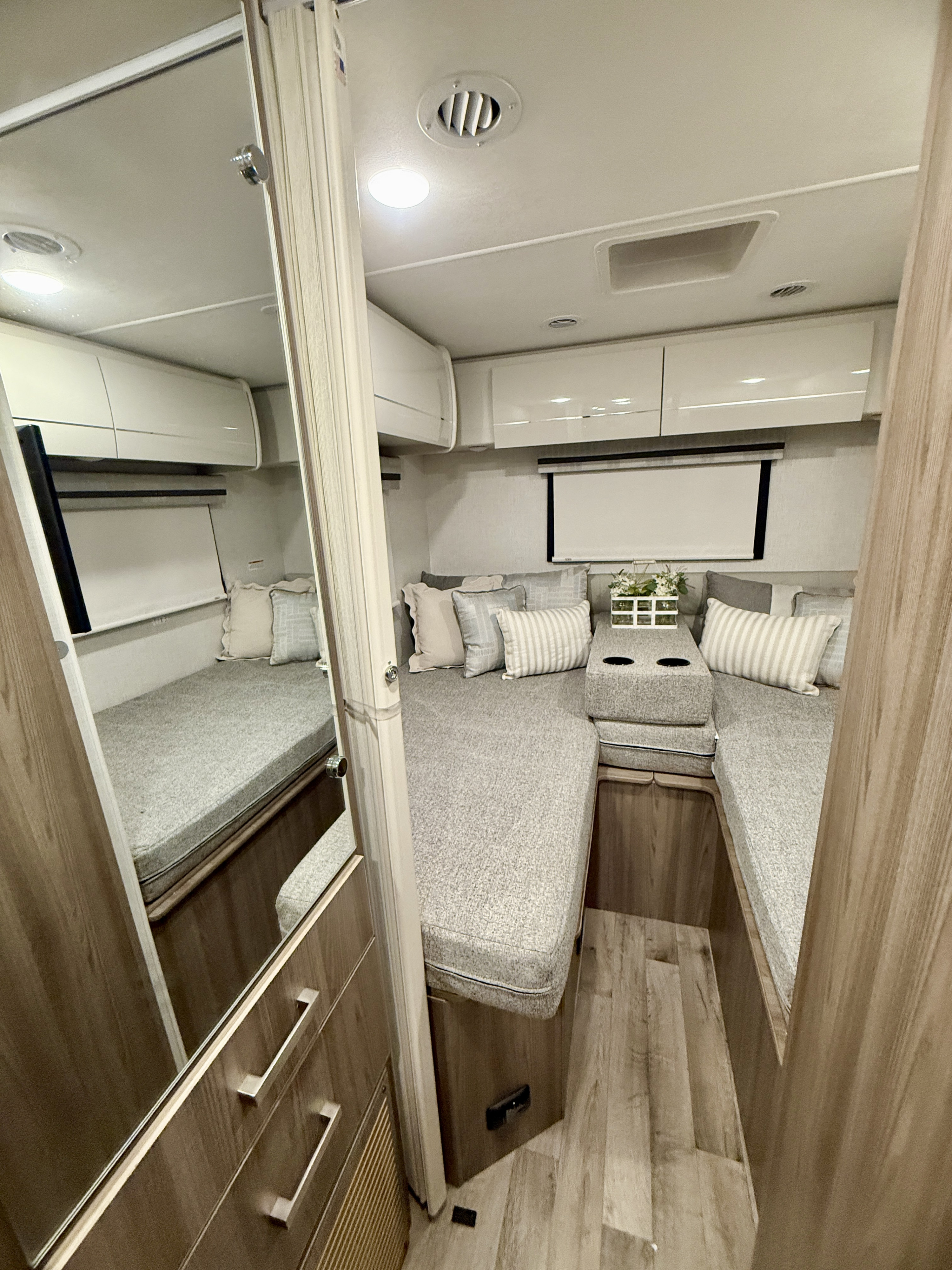 Modern RV rental interior featuring a bright dinette area with light gray cushions, convertible into a bed, and ample overhead storage.. Thor Motorcoach Vegas 2025