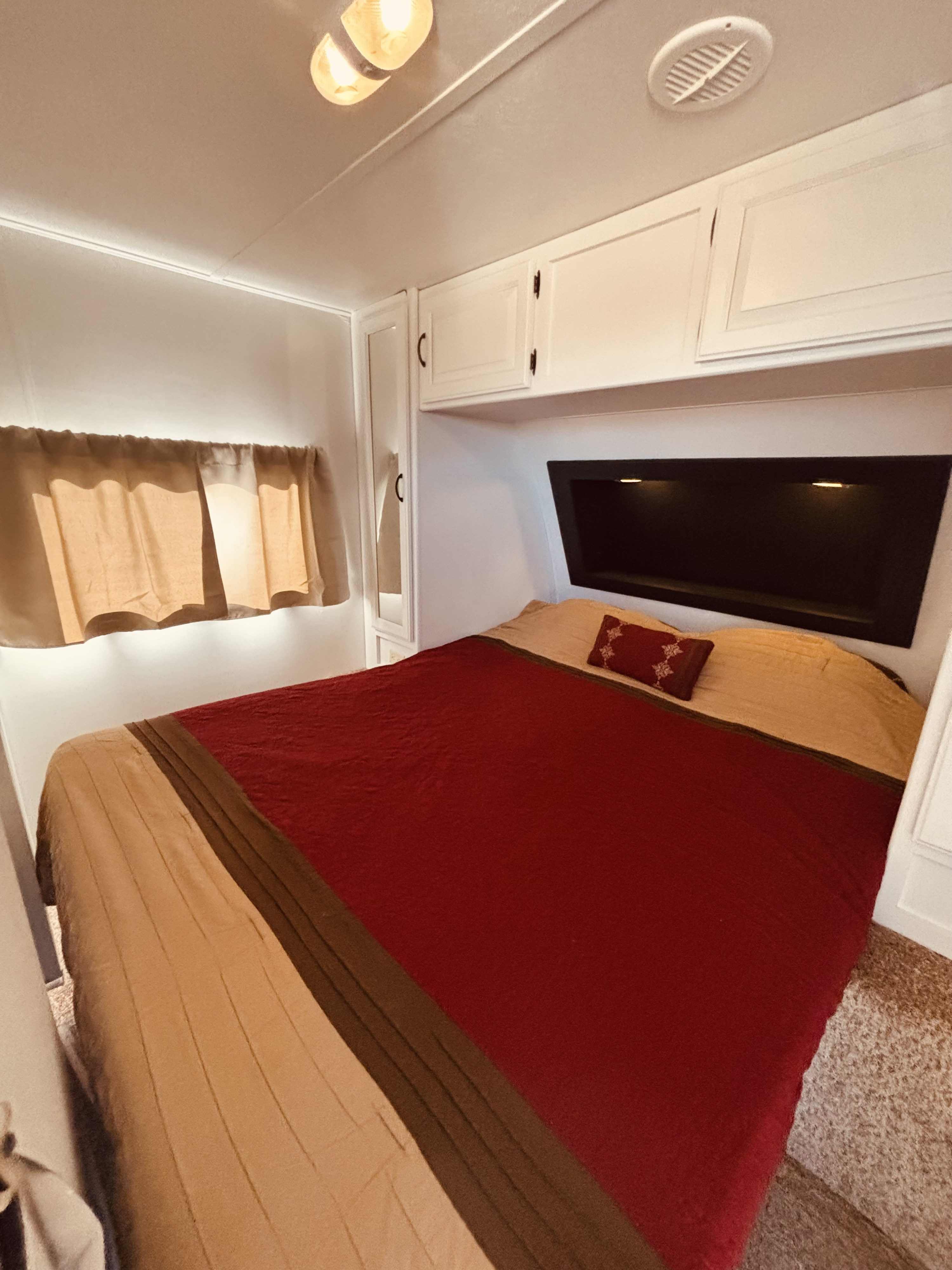 Cozy RV rental bedroom with a comfy bed, red comforter, overhead storage, and soft lighting for travel comfort.. Keystone RV Laredo 2013