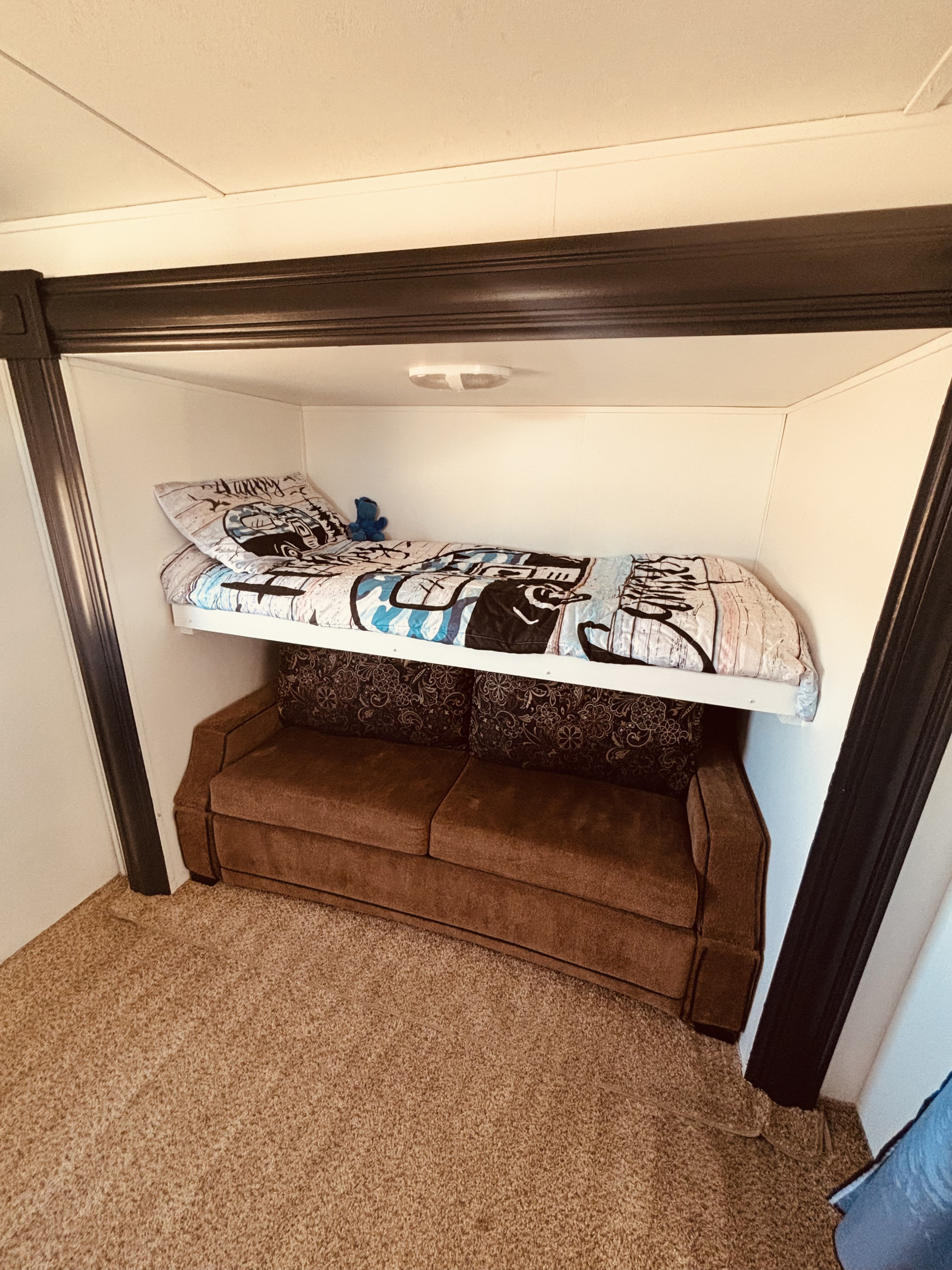 Inside an RV rental: a twin bunk bed with patterned bedding over a brown sofa, providing compact sleeping and seating.. Keystone RV Laredo 2013