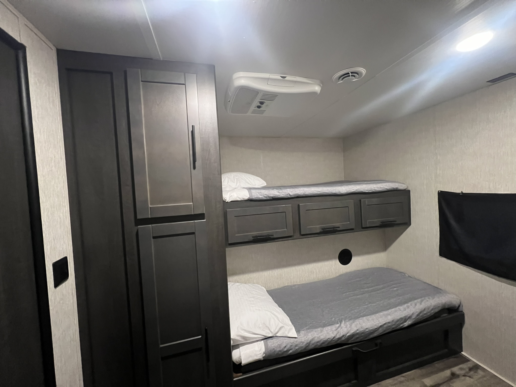 RV rental camper bunk beds with grey bedding, white pillows, overhead cabinets, AC, and a dark wardrobe.. Crossroads RV Cruiser Aire 2022