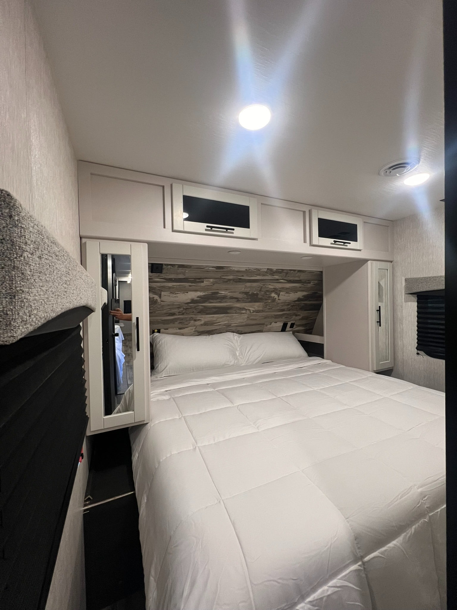 This cozy RV rental bedroom features a comfy bed with white bedding, overhead storage, and stylish wood-paneled headboard.. Crossroads RV Cruiser Aire 2022