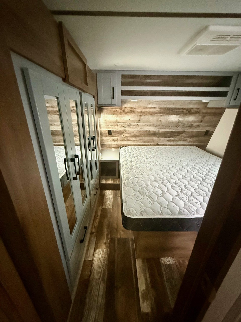 Spacious RV rental bedroom with a comfortable bed, mirrored closet, and modern wood-look interior for your next adventure.. Keystone Fuzion 2020