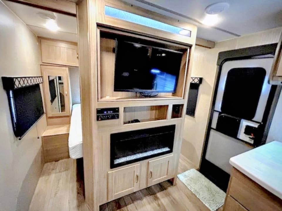 Modern **rv rental** interior showing entertainment system, electric fireplace, entry door, and a glimpse of the bedroom.. Coachmen Other 2020