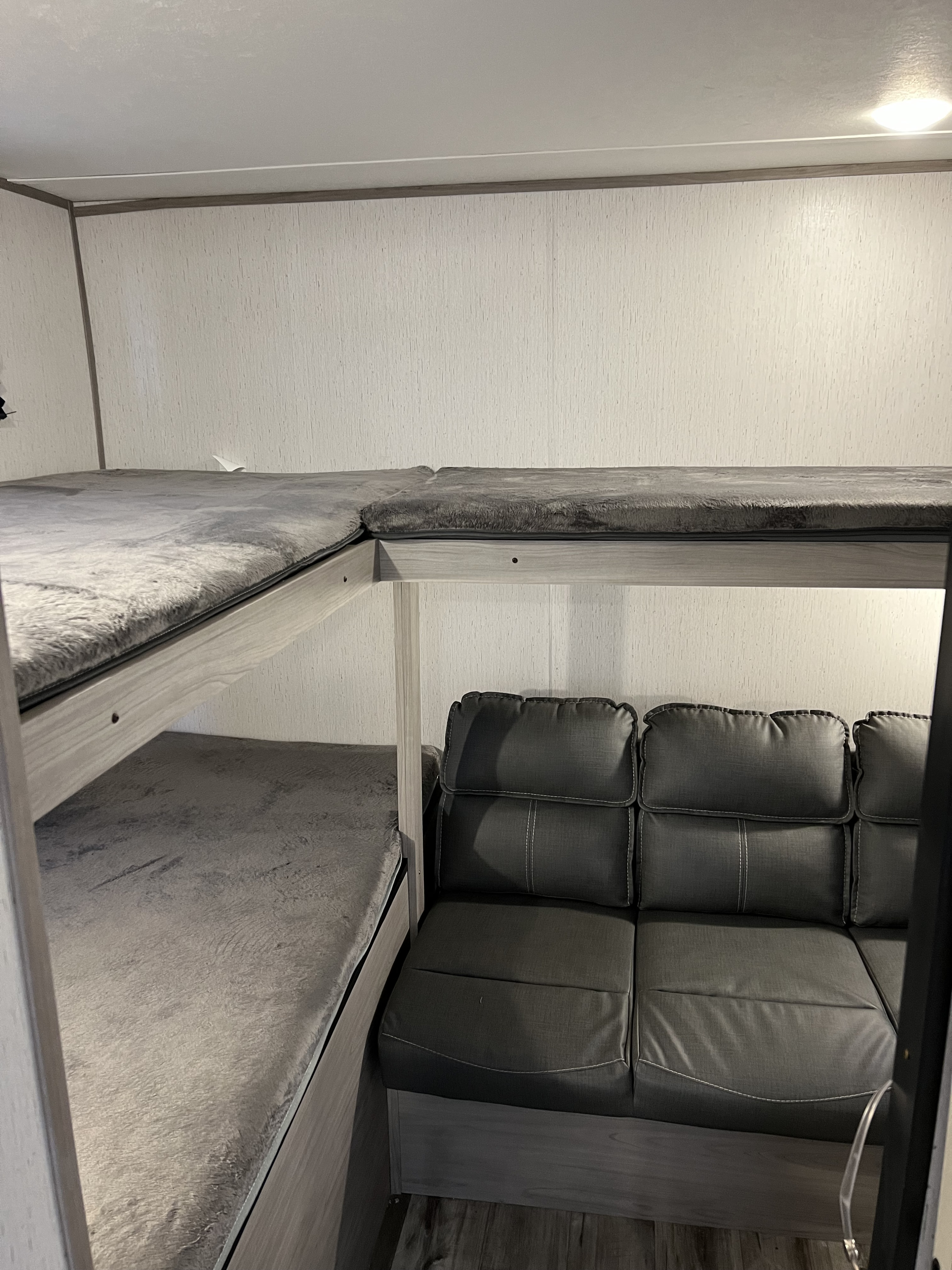 Inside an RV rental: gray bunk beds for sleeping and a matching sofa for lounging, optimizing space.. Dutchmen Coleman Lantern 2022