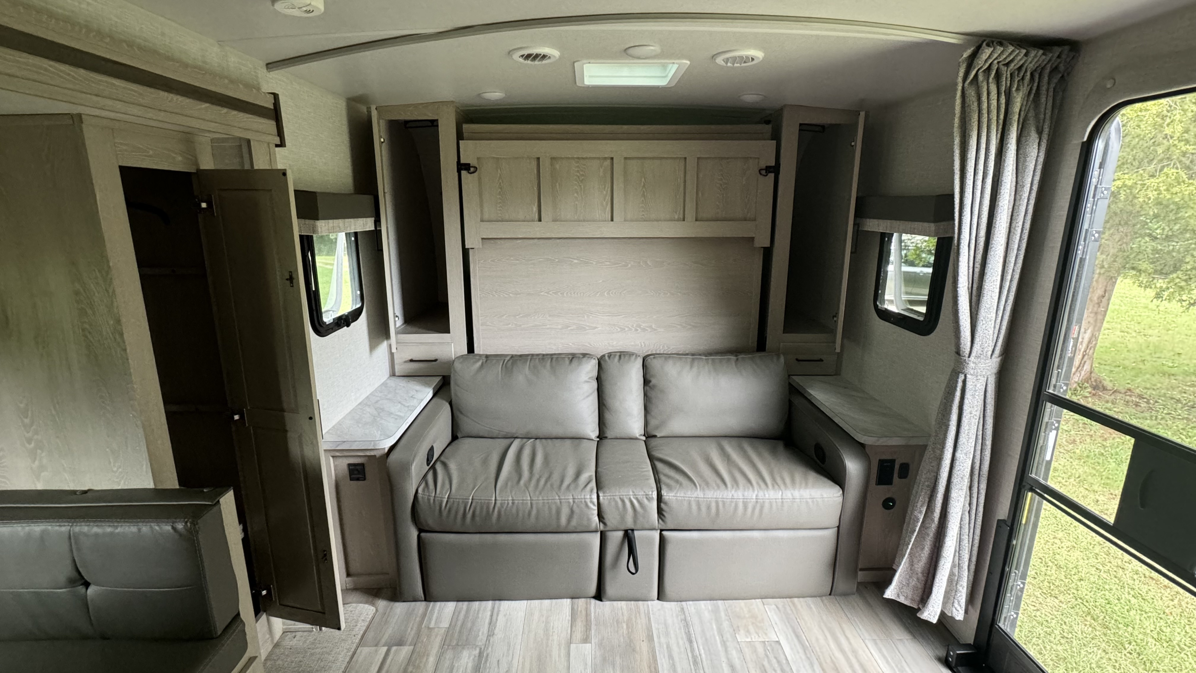 Inside a stylish RV rental: a gray convertible couch with an integrated murphy bed, overhead storage, and windows.. Forest River Flagstaff Micro Lite 2023