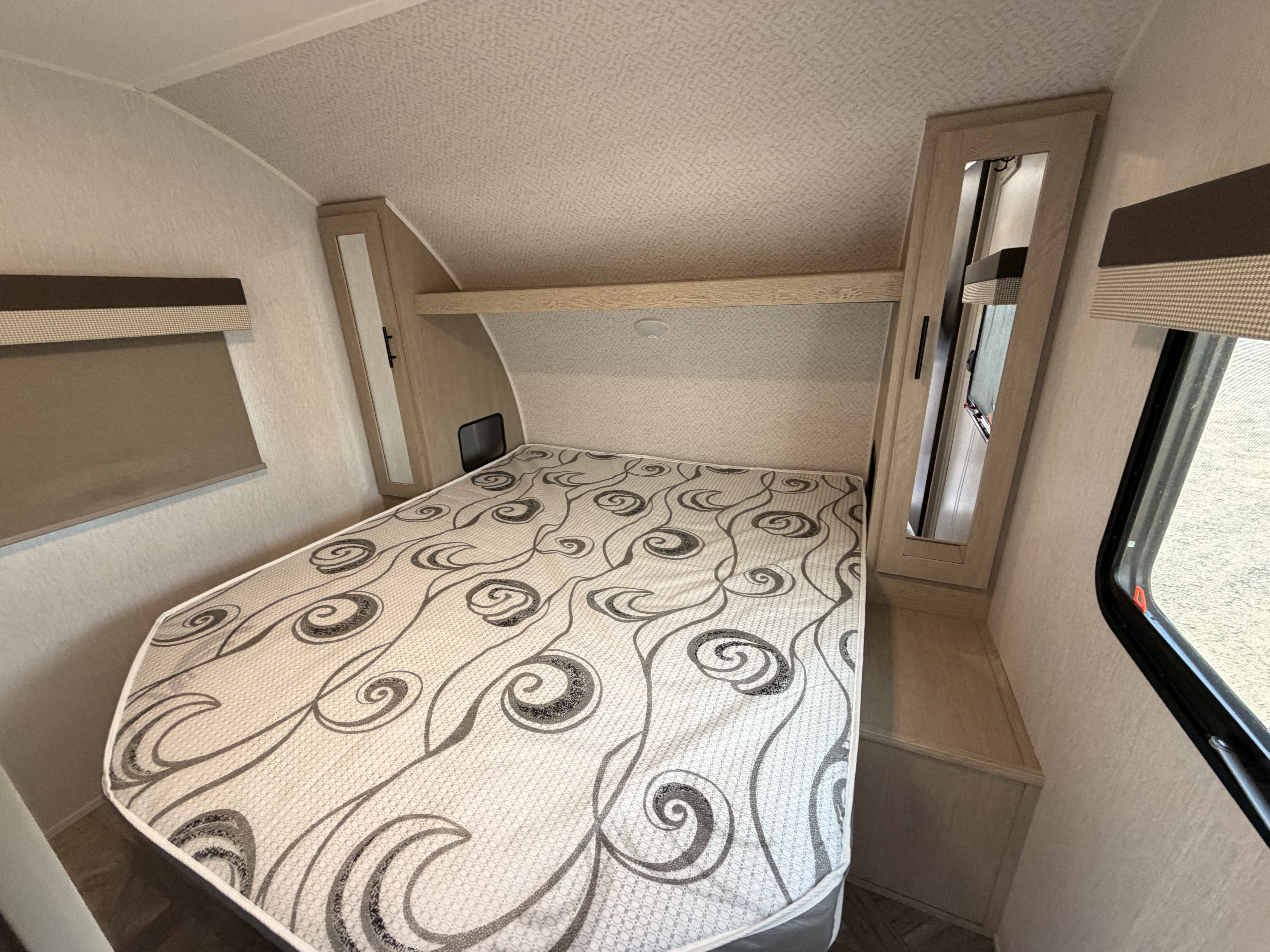 Modern rv rental bedroom with a patterned bed, mirrored wardrobes, textured walls/ceiling, and overhead storage.. Forest River Wildwood X-Lite Platinum 2024