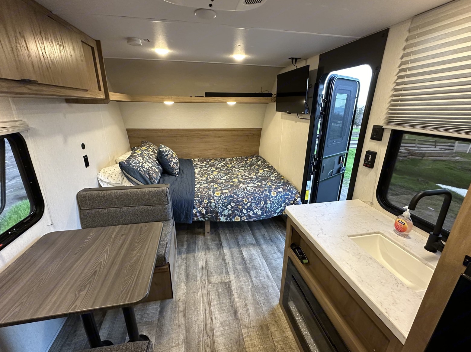 RV rental interior: cozy bed, dinette seating, and kitchen counter with sink. Open door beckons for travel.. Forest River Cherokee Wolf Den 16 EV 2024