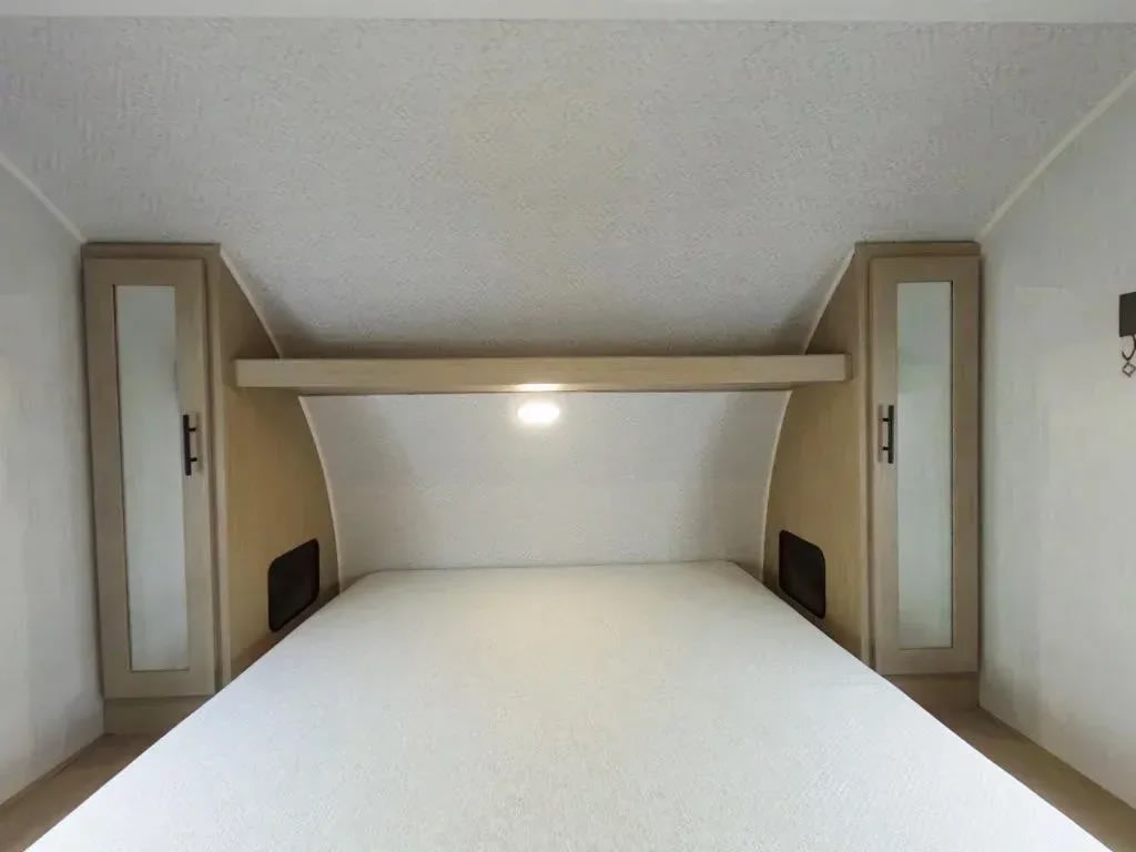 RV rental bedroom featuring a clean white mattress, light wood overhead storage with mirrored doors, and a centered reading light.. Forest River Evo 2750QBX 2023
